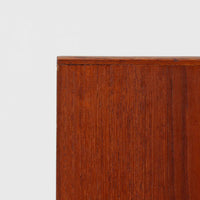 チーク材の豊かな木目が美しいこちらのサイドチェストは、北欧ビンテージらしい端正なデザインと実用性を兼ね備えた一台です。天板の縁には立ち上がりが施され、小物の転落を防ぐ工夫がされています。引き出し下のオープンスペースは本や雑貨の収納に便利で、ソファやベッドサイドに置けばサイドテーブルとしても活躍します。丸みを帯びた持ち手やテーパードレッグが柔らかな印象を与え、経年変化による木肌の深みが空間に温もりを添える逸品です。