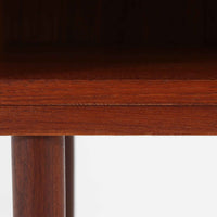 チーク材の豊かな木目が美しいこちらのサイドチェストは、北欧ビンテージらしい端正なデザインと実用性を兼ね備えた一台です。天板の縁には立ち上がりが施され、小物の転落を防ぐ工夫がされています。引き出し下のオープンスペースは本や雑貨の収納に便利で、ソファやベッドサイドに置けばサイドテーブルとしても活躍します。丸みを帯びた持ち手やテーパードレッグが柔らかな印象を与え、経年変化による木肌の深みが空間に温もりを添える逸品です。