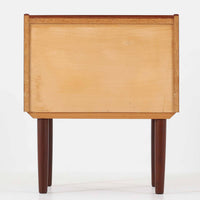 チーク材の豊かな木目が美しいこちらのサイドチェストは、北欧ビンテージらしい端正なデザインと実用性を兼ね備えた一台です。天板の縁には立ち上がりが施され、小物の転落を防ぐ工夫がされています。引き出し下のオープンスペースは本や雑貨の収納に便利で、ソファやベッドサイドに置けばサイドテーブルとしても活躍します。丸みを帯びた持ち手やテーパードレッグが柔らかな印象を与え、経年変化による木肌の深みが空間に温もりを添える逸品です。