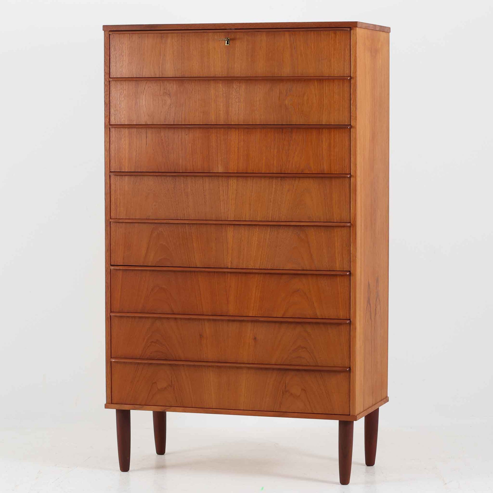 デンマーク製の8段チェストで、上質なチーク材の木目が存在感を放つ北欧ビンテージらしい一品です。細身の脚部に支えられた軽やかな佇まいと、北欧家具らしいバータイプの取っ手が、すっきりとした印象を与えます。衣類や小物をたっぷり収納でき、寝室やリビングで圧迫感なく使える点も魅力です。経年により深みを増した色艶が空間を温かく彩り、実用性と美しさを兼ね備えたチェストで、デンマークでも8段タイプは流通が少なく希少なモデルです。