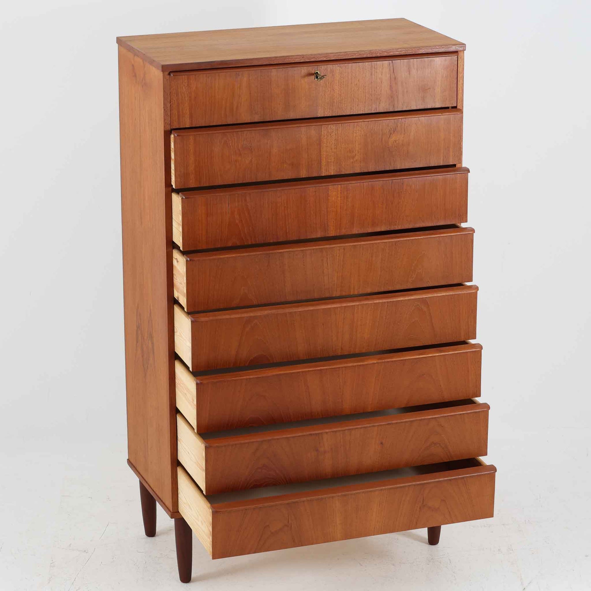 デンマーク製の8段チェストで、上質なチーク材の木目が存在感を放つ北欧ビンテージらしい一品です。細身の脚部に支えられた軽やかな佇まいと、北欧家具らしいバータイプの取っ手が、すっきりとした印象を与えます。衣類や小物をたっぷり収納でき、寝室やリビングで圧迫感なく使える点も魅力です。経年により深みを増した色艶が空間を温かく彩り、実用性と美しさを兼ね備えたチェストで、デンマークでも8段タイプは流通が少なく希少なモデルです。