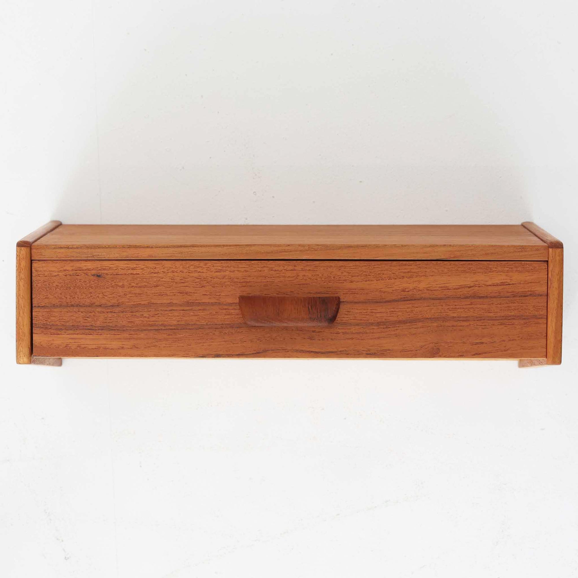 壁付け仕様のこちらのウォールシェルフは、上質なチーク材を用いた北欧ビンテージ家具で、直線的なフォルムと程よい奥行きが特徴です。引き出し収納を備えており、小物や手元のアイテムをすっきりと整理できる実用性も兼ね備えています。ミニマルなデザインながらも丁寧な仕上げが施されており、玄関先やベッドサイド、リビングのアクセントとしても活躍します。経年によって深まったチークの風合いが空間に落ち着いた温もりを添える一点です。