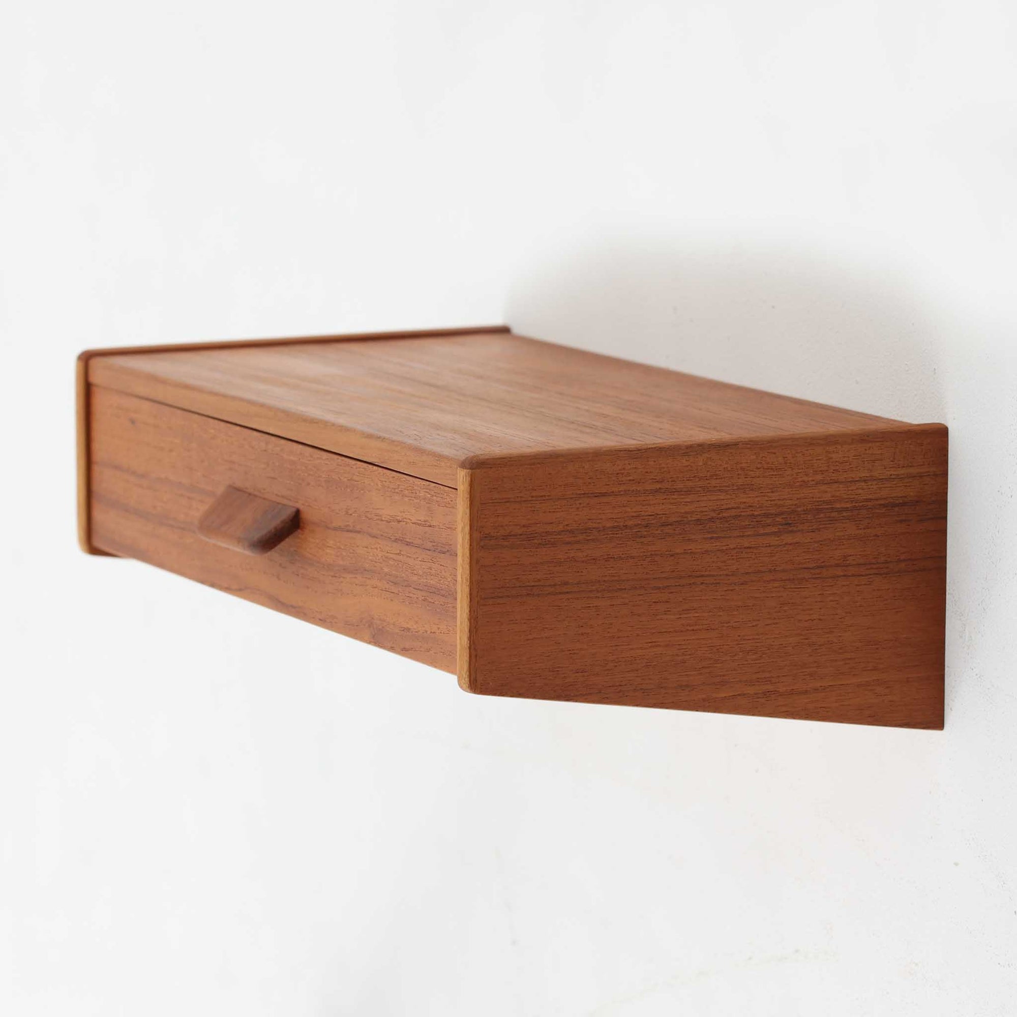壁付け仕様のこちらのウォールシェルフは、上質なチーク材を用いた北欧ビンテージ家具で、直線的なフォルムと程よい奥行きが特徴です。引き出し収納を備えており、小物や手元のアイテムをすっきりと整理できる実用性も兼ね備えています。ミニマルなデザインながらも丁寧な仕上げが施されており、玄関先やベッドサイド、リビングのアクセントとしても活躍します。経年によって深まったチークの風合いが空間に落ち着いた温もりを添える一点です。