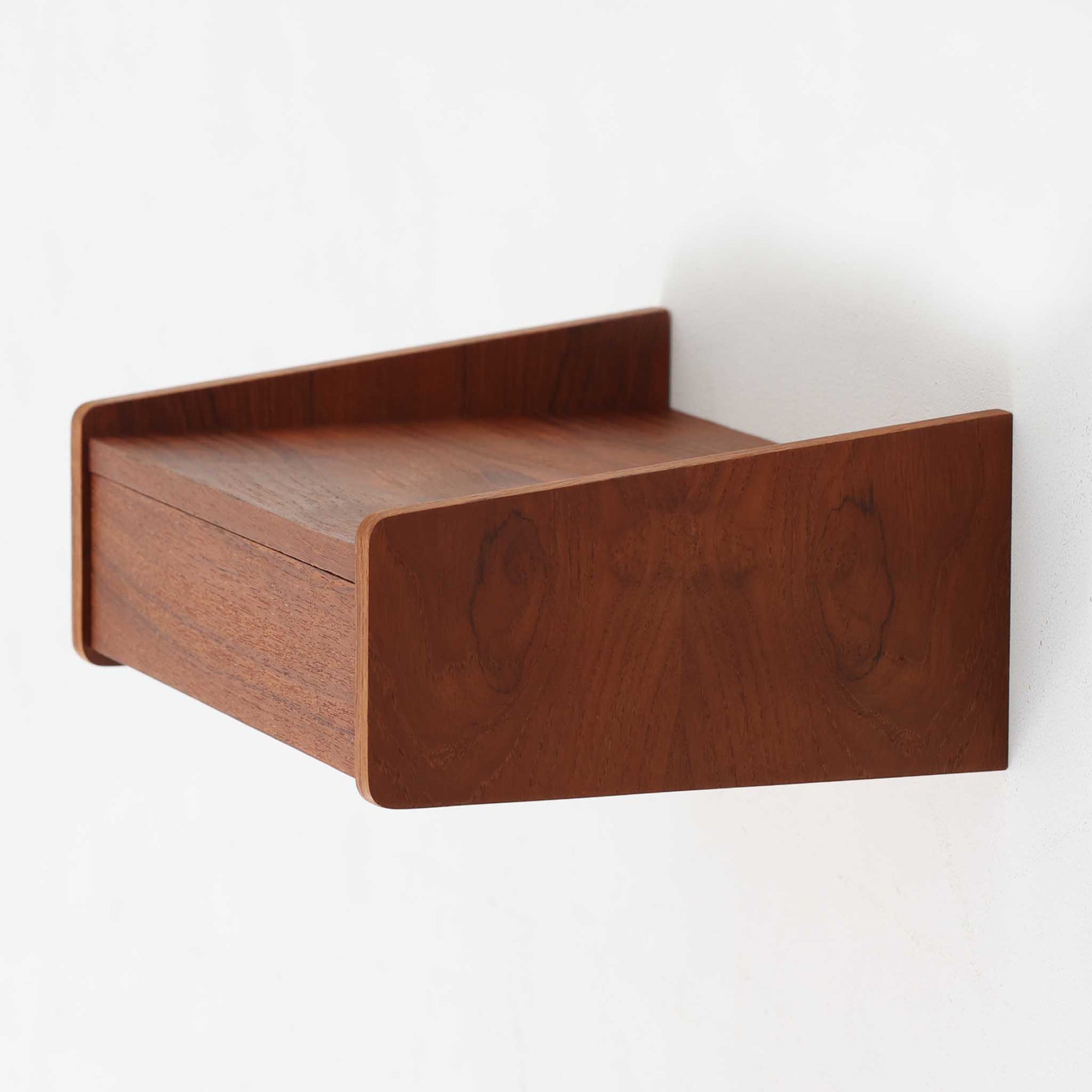 チーク材を使用したこちらのウォールシェルフは、立ち上がりの付いたサイドパネルが滑らかな曲線を描く、美しいシルエットが魅力の北欧ビンテージ家具です。壁面に取り付けることで省スペースながらも収納力を確保でき、ベッドサイドや玄関、リビングのアクセントとして活躍します。背面構造からビスでの取り付け仕様となっており、取り付け跡や構造の素朴さからも当時の職人仕事の温もりが感じられます。小ぶりながらも素材の魅力と機能性を備えた一品です。