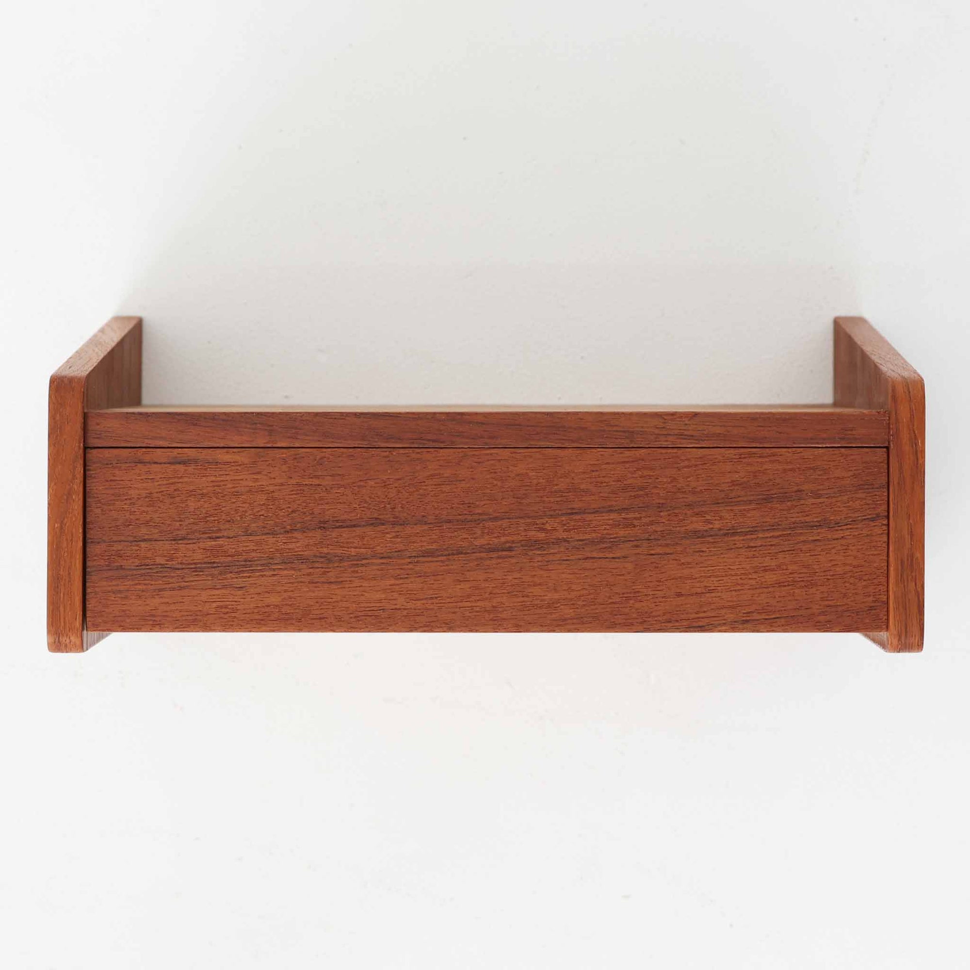 チーク材を使用したこちらのウォールシェルフは、立ち上がりの付いたサイドパネルが滑らかな曲線を描く、美しいシルエットが魅力の北欧ビンテージ家具です。壁面に取り付けることで省スペースながらも収納力を確保でき、ベッドサイドや玄関、リビングのアクセントとして活躍します。背面構造からビスでの取り付け仕様となっており、取り付け跡や構造の素朴さからも当時の職人仕事の温もりが感じられます。小ぶりながらも素材の魅力と機能性を備えた一品です。