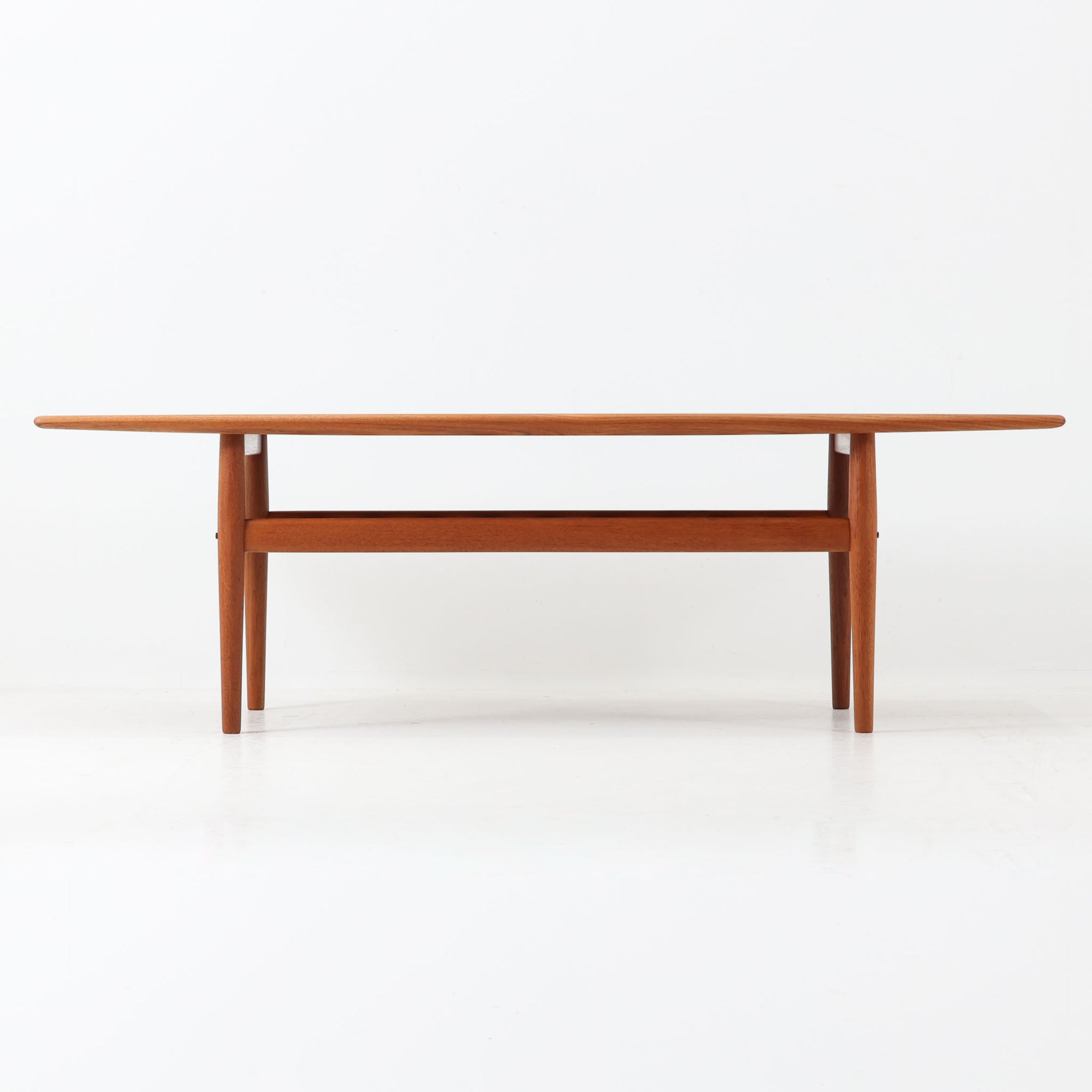 Grete Jalkがデザインし、Glostrup Mobelfabrikで製作されたこちらのセンターテーブルは、端正なプロポーションと軽やかな構造が魅力の北欧ビンテージ品です。幅160cmのゆとりある天板下にはスラット状の棚板を備え、雑誌やブランケットなどを整理しながら使える実用性も兼ね備えています。丸みを帯びた脚部や天板縁の丁寧な仕上げからは、女性デザイナーらしい繊細な美意識と当時の高い木工技術が感じられ、経年により深みを増した木肌が空間に落ち着いた存在感をもたらします。