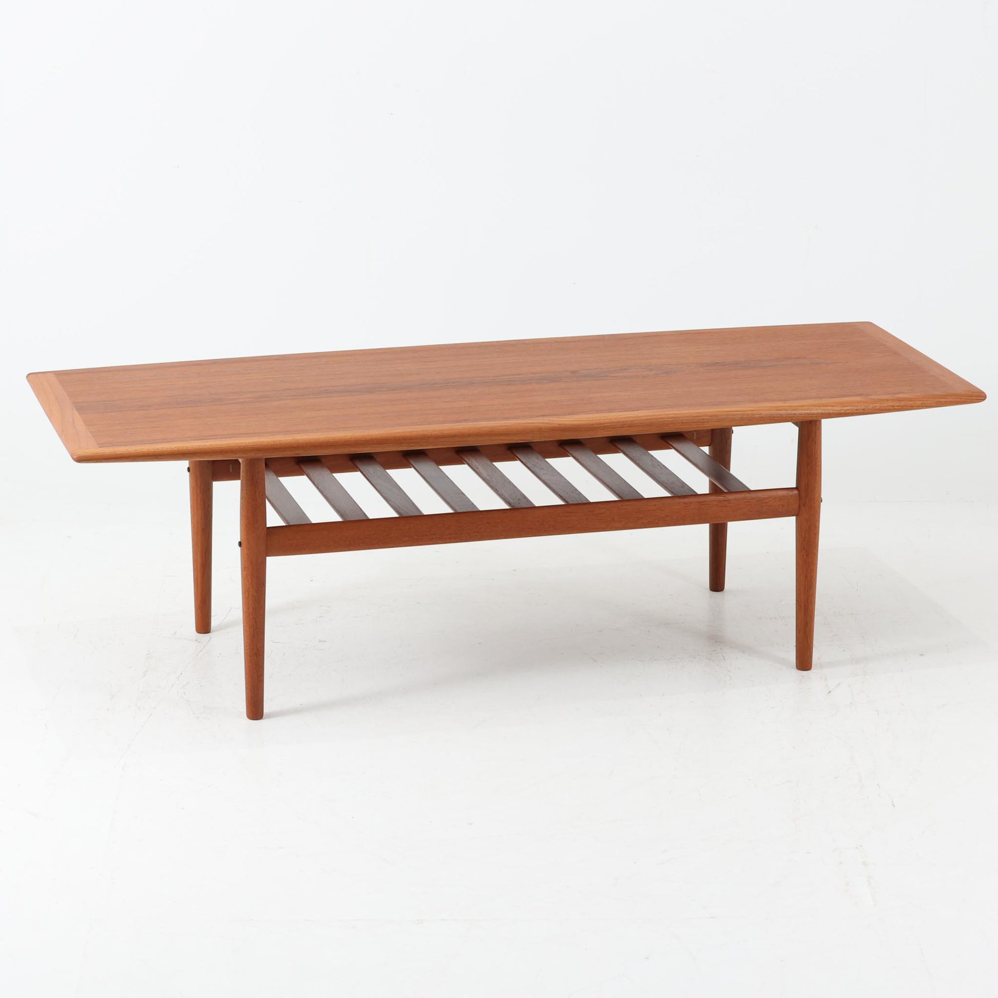 Grete Jalkがデザインし、Glostrup Mobelfabrikで製作されたこちらのセンターテーブルは、端正なプロポーションと軽やかな構造が魅力の北欧ビンテージ品です。幅160cmのゆとりある天板下にはスラット状の棚板を備え、雑誌やブランケットなどを整理しながら使える実用性も兼ね備えています。丸みを帯びた脚部や天板縁の丁寧な仕上げからは、女性デザイナーらしい繊細な美意識と当時の高い木工技術が感じられ、経年により深みを増した木肌が空間に落ち着いた存在感をもたらします。