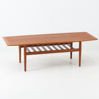 Grete Jalkがデザインし、Glostrup Mobelfabrikで製作されたこちらのセンターテーブルは、端正なプロポーションと軽やかな構造が魅力の北欧ビンテージ品です。幅160cmのゆとりある天板下にはスラット状の棚板を備え、雑誌やブランケットなどを整理しながら使える実用性も兼ね備えています。丸みを帯びた脚部や天板縁の丁寧な仕上げからは、女性デザイナーらしい繊細な美意識と当時の高い木工技術が感じられ、経年により深みを増した木肌が空間に落ち着いた存在感をもたらします。