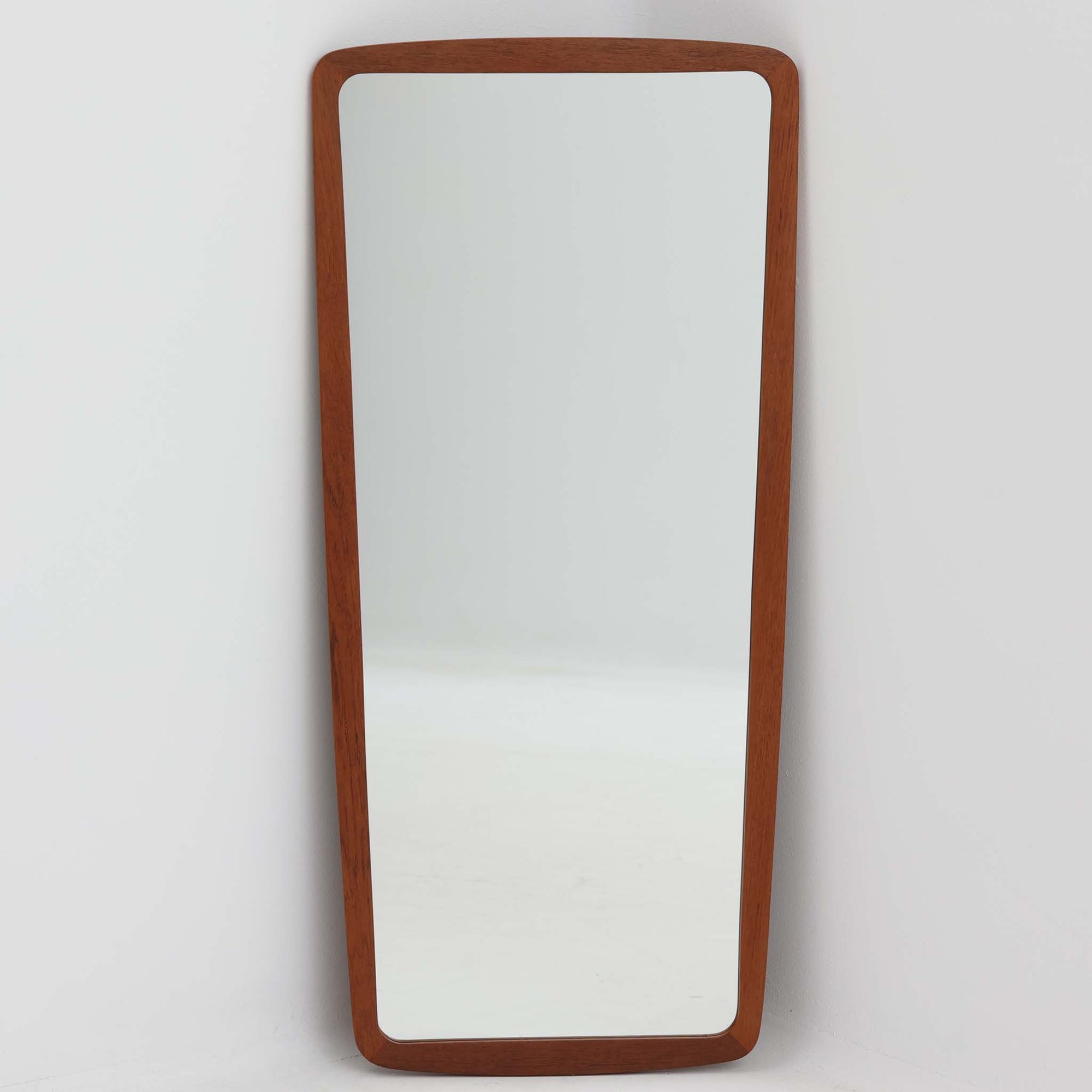 デンマーク製壁掛け／立掛けミラーです。チーク材のフレームは角に丸みをもたせた柔らかなデザインで、北欧らしいシンプルで温かみのある雰囲気を漂わせます。無駄のない細身のフレームが鏡面を引き立て、空間を広く明るく見せてくれます。壁に掛けても、床に立て掛けても美しく、玄関や寝室などさまざまなシーンで活躍します。経年により深みを増した木肌が味わい深く、北欧ビンテージならではの上質な存在感を放つ一品です。