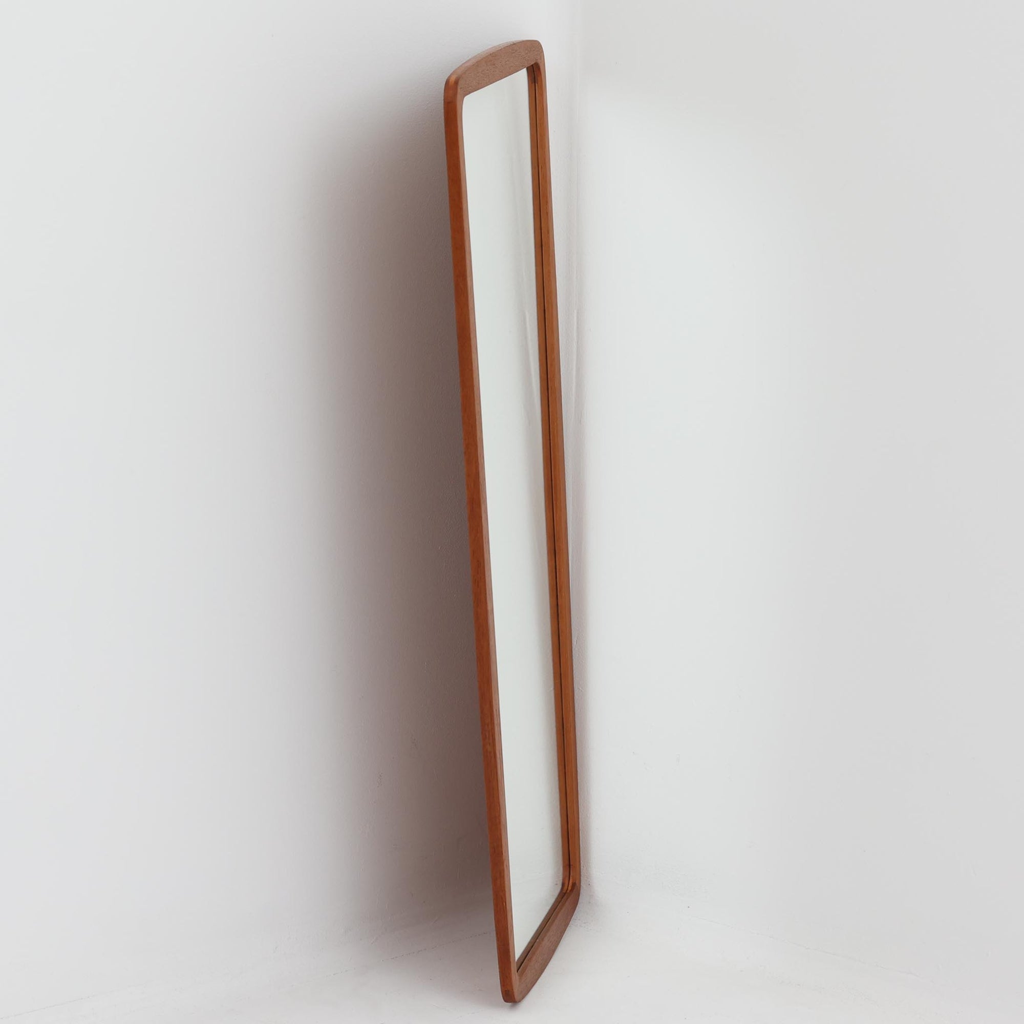 デンマーク製壁掛け／立掛けミラーです。チーク材のフレームは角に丸みをもたせた柔らかなデザインで、北欧らしいシンプルで温かみのある雰囲気を漂わせます。無駄のない細身のフレームが鏡面を引き立て、空間を広く明るく見せてくれます。壁に掛けても、床に立て掛けても美しく、玄関や寝室などさまざまなシーンで活躍します。経年により深みを増した木肌が味わい深く、北欧ビンテージならではの上質な存在感を放つ一品です。