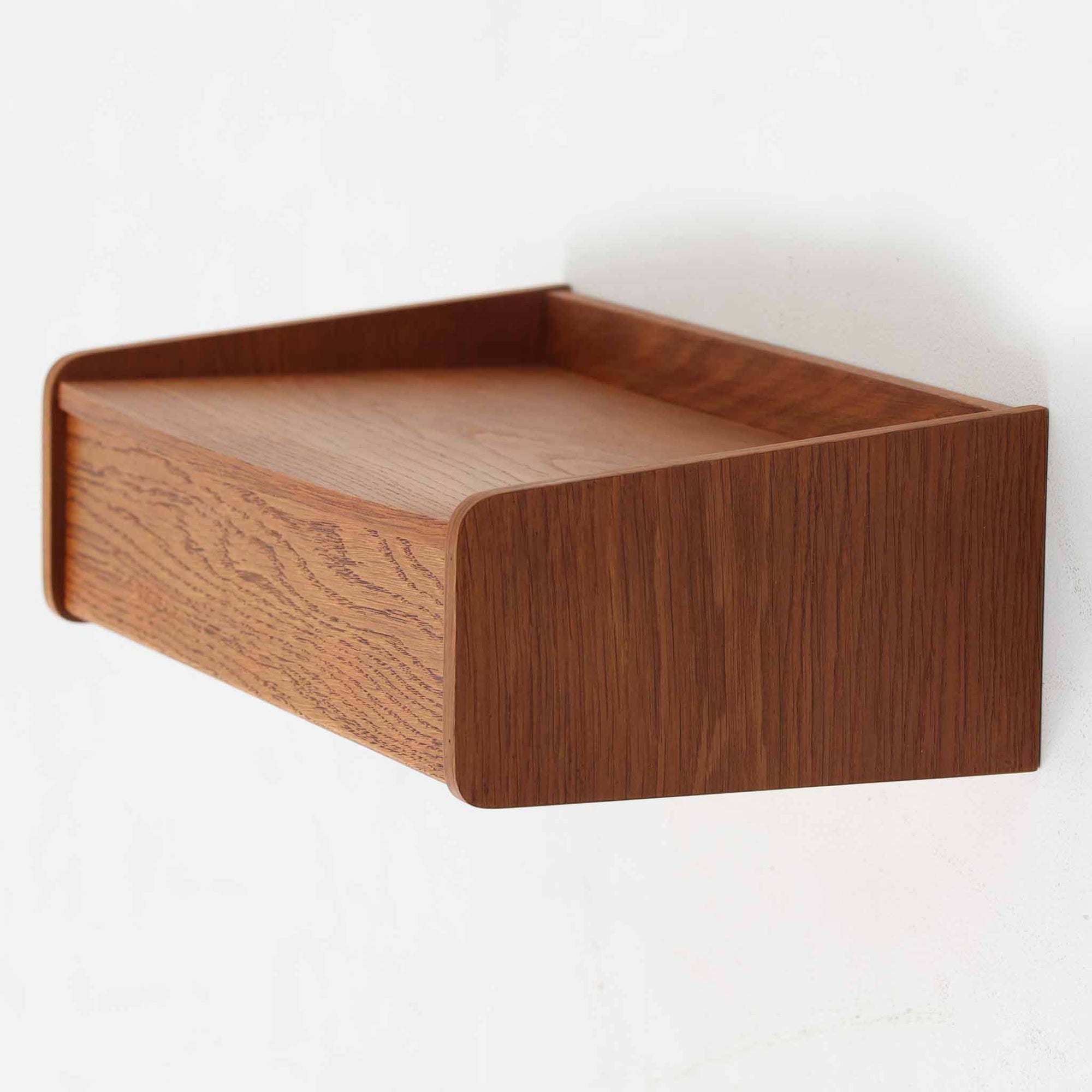 すっきりとした直線構成が印象的なこちらのウォールシェルフは、チーク材を使用した北欧ビンテージ家具で、あたたかみのある木目と美しい色合いが魅力です。緩やかにカーブしたサイドパネルの立ち上がりがデザインのアクセントとなっており、シンプルながらも洗練された佇まいを感じさせます。背面には取り付け穴が設けられており、壁面にしっかりと固定できる構造です。玄関や寝室など、限られたスペースでも活躍する実用性と美しさを兼ね備えた一台です。