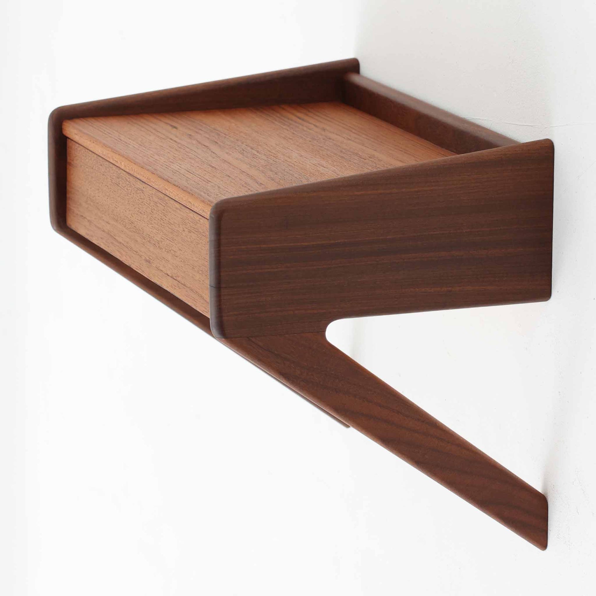 デンマーク製のチーク材ウォールシェルフで、シンプルながら洗練されたデザインが魅力の北欧ビンテージ家具です。壁付けタイプで引き出しを備えており、小物収納としても実用的です。前面や側面は柔らかな曲線を取り入れた造形で、温かみあるチーク材の質感と相まって上品な存在感を放ちます。寝室のベッドサイドや玄関の小物置きとしても活躍し、コンパクトながら空間を引き締めるアクセントになります。経年による風合いが味わいを深め、北欧家具らしい魅力を存分に感じられる一品です。