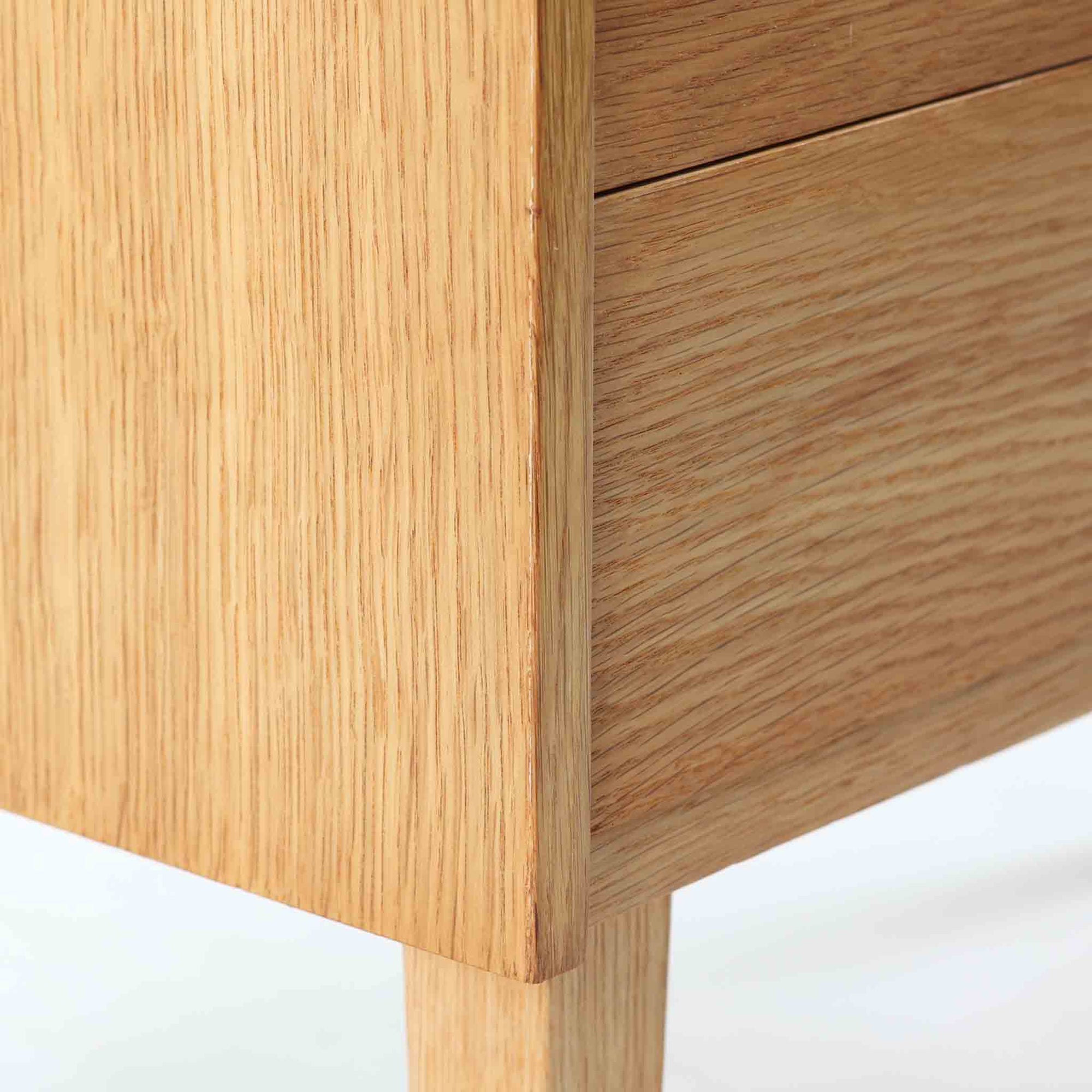 オーク材を用いたこちらの2段チェストは、北欧ビンテージ家具らしいシンプルかつ機能的なデザインが魅力です。直線的なフォルムに対し、細身でテーパーのかかった脚部が軽やかな印象を与え、空間を圧迫せずに置くことができます。幅60cmとコンパクトながら、2杯の引き出しは日用品や小物収納に便利で、ベッドサイドやリビングの補助収納としても最適です。経年により深みを増したオークの木肌が、温もりある雰囲気を演出する一点物です。