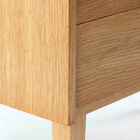 オーク材を用いたこちらの2段チェストは、北欧ビンテージ家具らしいシンプルかつ機能的なデザインが魅力です。直線的なフォルムに対し、細身でテーパーのかかった脚部が軽やかな印象を与え、空間を圧迫せずに置くことができます。幅60cmとコンパクトながら、2杯の引き出しは日用品や小物収納に便利で、ベッドサイドやリビングの補助収納としても最適です。経年により深みを増したオークの木肌が、温もりある雰囲気を演出する一点物です。