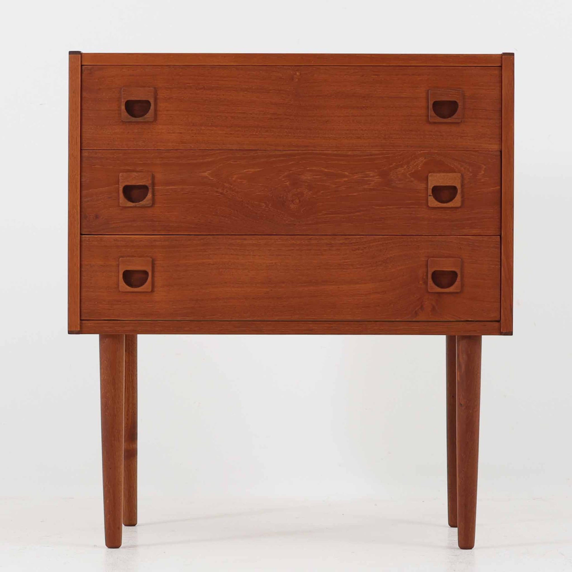 デンマーク製のチーク材を使用した3段チェストです。コンパクトな幅62cmのサイズ感ながら、3杯の引き出しを備え収納力に優れており、リビングや寝室、玄関先など幅広いシーンで活躍します。スクエア型の取っ手は彫り込みデザインで指掛かりが良く、シンプルながらも北欧家具らしい温もりと実用性を感じさせます。経年により深みを増したチーク材の色合いが、空間に落ち着きと上質な雰囲気をもたらし、ビンテージならではの魅力を楽しめる一台です。