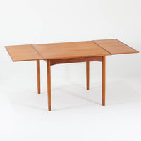 北欧らしい実用性と素材の良さが感じられる正方形エクステンションテーブルです。天板には良質なチーク材が用いられ、赤みのある木目と滑らかな手触りが、経年変化による深みとともに味わいを増しています。通常時はコンパクトなサイズ感で使いやすく、左右の補助天板を引き出すことで来客時や食事人数に応じて柔軟に対応できる構造です。脚部は細身で圧迫感がなく、幕板の緩やかな曲線が全体にやわらかな印象を与え、ダイニングはもちろんワークテーブルとしてもおすすめです。