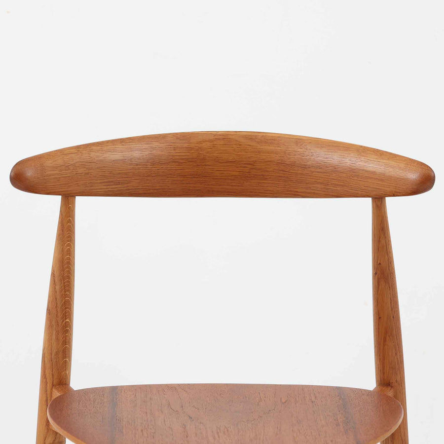 Hans J. Wegnerがデザインし、Fritz Hansen社より発表されたFH4103チェアは、三角形に近い座面と滑らかな曲線を描く笠木が特徴の北欧ビンテージ家具です。フレームには堅牢なオーク材、座面には温かみあるチーク材を組み合わせ、素材のコントラストが美しいバランスを生み出しています。彫刻的なフォルムながら軽やかで実用的な構造は、ダイニングチェアとしてはもちろん、空間のアクセントピースとしても存在感を放ちます。経年による木肌の深い風合いが、ビンテージならではの魅力を引き立てています。