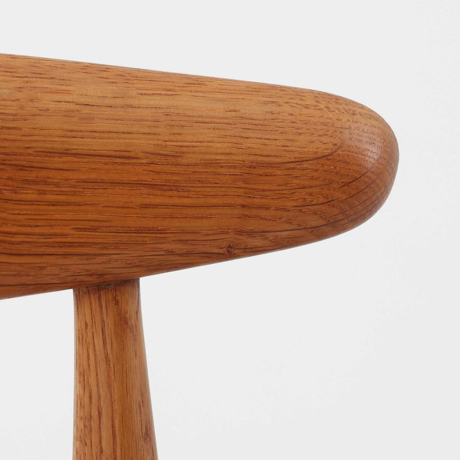 Hans J. Wegnerがデザインし、Fritz Hansen社より発表されたFH4103チェアは、三角形に近い座面と滑らかな曲線を描く笠木が特徴の北欧ビンテージ家具です。フレームには堅牢なオーク材、座面には温かみあるチーク材を組み合わせ、素材のコントラストが美しいバランスを生み出しています。彫刻的なフォルムながら軽やかで実用的な構造は、ダイニングチェアとしてはもちろん、空間のアクセントピースとしても存在感を放ちます。経年による木肌の深い風合いが、ビンテージならではの魅力を引き立てています。