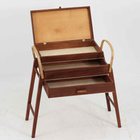 こちらのソーイングボックスは、チーク材とビーチ材を組み合わせた軽やかな構成が魅力の北欧ビンテージ品で、トップのフラップを開くと段違いに展開するトレイと下段の引き出しが現れる優れた収納構造を備え、裁縫道具や小物を効率よく整理できます。柔らかく曲げられた左右のビーチ材の持ち手がアクセントとなり、職人技の感じられる繊細な作りと経年で深まった木肌の風合いが空間に温かな存在感をもたらします。リビングやワークスペースのサイドテーブルとしても実用的にお使いいただけます。