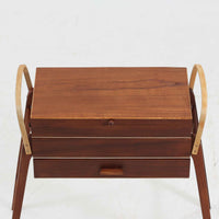 こちらのソーイングボックスは、チーク材とビーチ材を組み合わせた軽やかな構成が魅力の北欧ビンテージ品で、トップのフラップを開くと段違いに展開するトレイと下段の引き出しが現れる優れた収納構造を備え、裁縫道具や小物を効率よく整理できます。柔らかく曲げられた左右のビーチ材の持ち手がアクセントとなり、職人技の感じられる繊細な作りと経年で深まった木肌の風合いが空間に温かな存在感をもたらします。リビングやワークスペースのサイドテーブルとしても実用的にお使いいただけます。