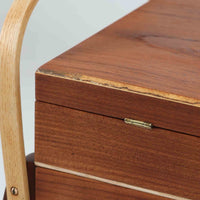 こちらのソーイングボックスは、チーク材とビーチ材を組み合わせた軽やかな構成が魅力の北欧ビンテージ品で、トップのフラップを開くと段違いに展開するトレイと下段の引き出しが現れる優れた収納構造を備え、裁縫道具や小物を効率よく整理できます。柔らかく曲げられた左右のビーチ材の持ち手がアクセントとなり、職人技の感じられる繊細な作りと経年で深まった木肌の風合いが空間に温かな存在感をもたらします。リビングやワークスペースのサイドテーブルとしても実用的にお使いいただけます。