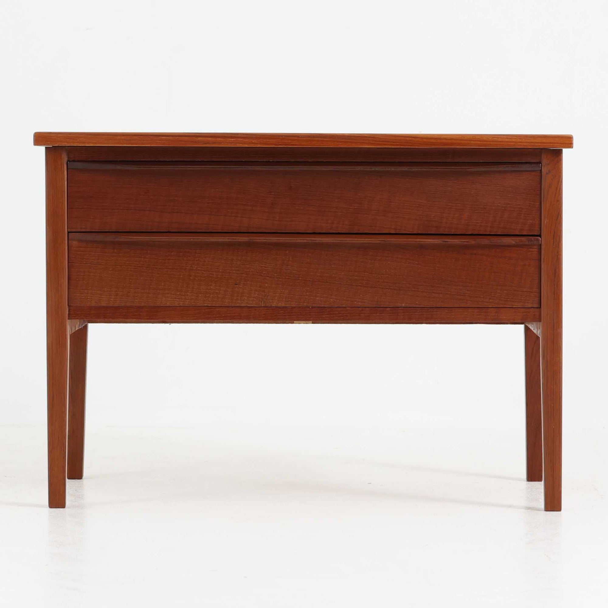 デンマーク製2段チェストです。無駄のないシンプルなフォルムとチーク材特有の深みのある色合いが美しく、北欧らしい上品な佇まいを感じさせます。引き出しの前板にはデンマーク家具らしい取手が施され、素材の質感を引き立てるデザインです。上段には仕切りが設けられており、小物の整理にも便利です。コンパクトなサイズながら収納力があり、リビングやベッドサイドなど幅広いシーンで活躍します。経年により艶を増した木肌が空間に温もりを添える一品です。