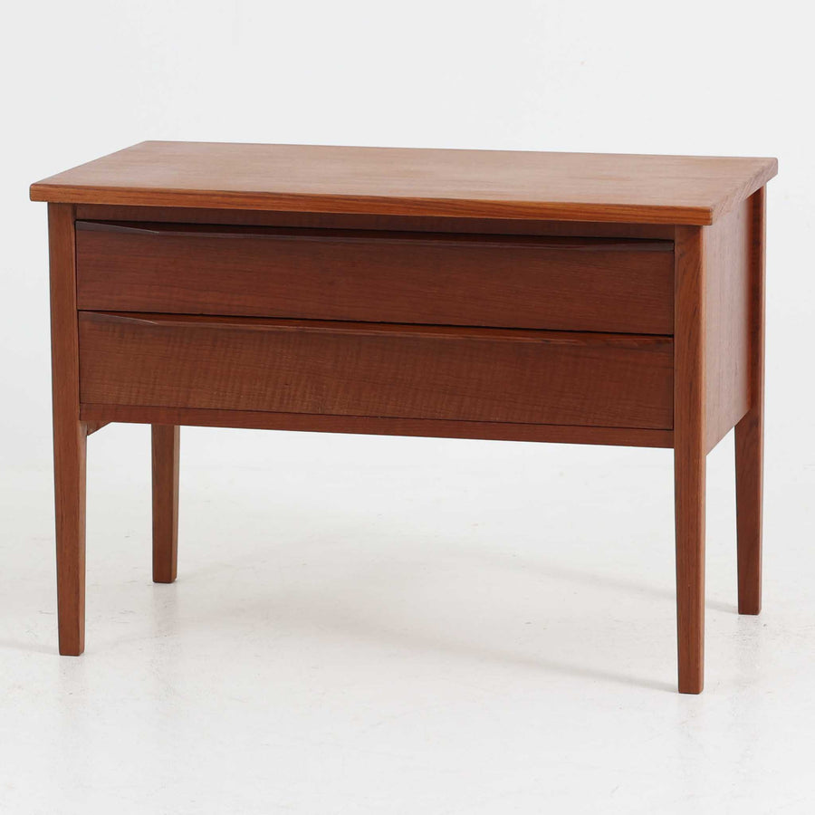 デンマーク製2段チェストです。無駄のないシンプルなフォルムとチーク材特有の深みのある色合いが美しく、北欧らしい上品な佇まいを感じさせます。引き出しの前板にはデンマーク家具らしい取手が施され、素材の質感を引き立てるデザインです。上段には仕切りが設けられており、小物の整理にも便利です。コンパクトなサイズながら収納力があり、リビングやベッドサイドなど幅広いシーンで活躍します。経年により艶を増した木肌が空間に温もりを添える一品です。