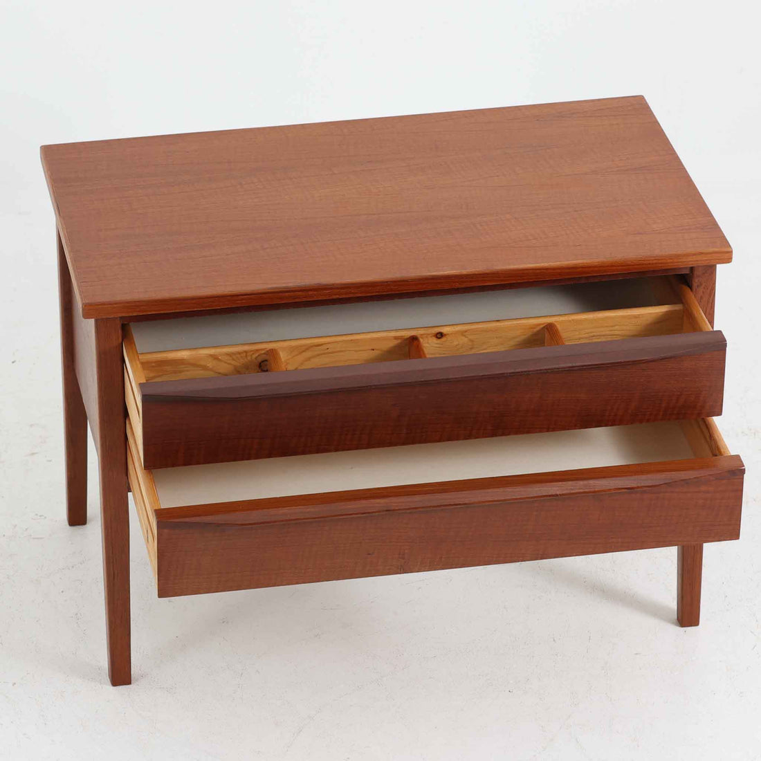 デンマーク製2段チェストです。無駄のないシンプルなフォルムとチーク材特有の深みのある色合いが美しく、北欧らしい上品な佇まいを感じさせます。引き出しの前板にはデンマーク家具らしい取手が施され、素材の質感を引き立てるデザインです。上段には仕切りが設けられており、小物の整理にも便利です。コンパクトなサイズながら収納力があり、リビングやベッドサイドなど幅広いシーンで活躍します。経年により艶を増した木肌が空間に温もりを添える一品です。