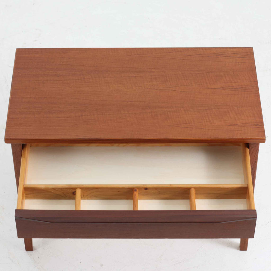 デンマーク製2段チェストです。無駄のないシンプルなフォルムとチーク材特有の深みのある色合いが美しく、北欧らしい上品な佇まいを感じさせます。引き出しの前板にはデンマーク家具らしい取手が施され、素材の質感を引き立てるデザインです。上段には仕切りが設けられており、小物の整理にも便利です。コンパクトなサイズながら収納力があり、リビングやベッドサイドなど幅広いシーンで活躍します。経年により艶を増した木肌が空間に温もりを添える一品です。