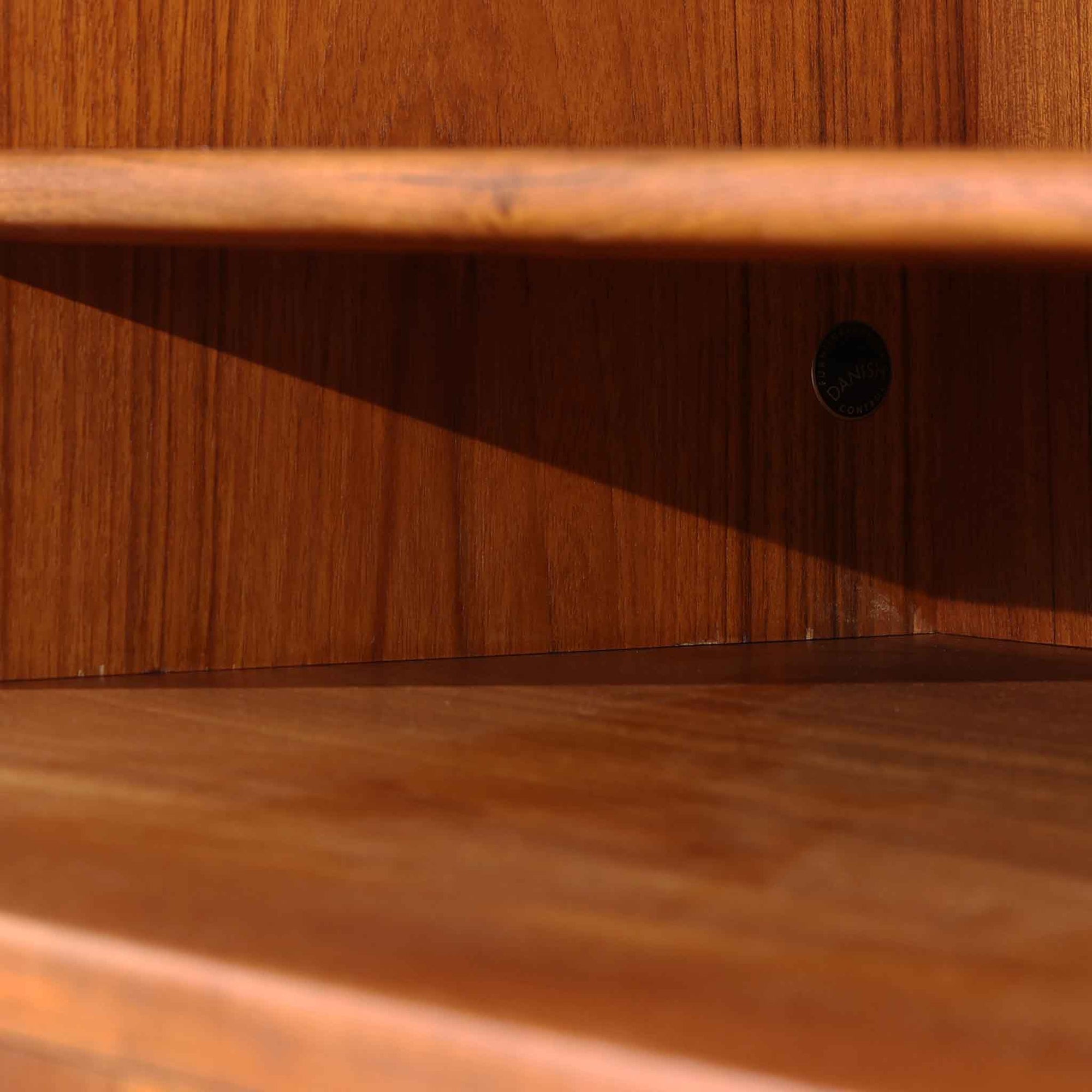 デンマークの巨匠Hans J. Wegner（ハンス・J・ウェグナー）がRY Mobler社のためにデザインしたディスプレイシェルフ「RY5 / RY15」です。上質なチーク材とオーク材を組み合わせ、下段収納部の取手には真鍮を用いた精緻なつくりが特徴です。シンプルながらも素材の美しさが際立ち、ウェグナーらしい温かみのあるデザインに仕上がっています。上段の棚は高さ調整が可能で、下段には仕切り付きの収納スペースを備え、実用性にも優れます。経年により深みを増した木肌の風合いが美しく、リビングや書斎で本や器を飾るなど、多用途に活躍する北欧ビンテージ家具です。