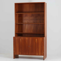 デンマークの巨匠Hans J. Wegner（ハンス・J・ウェグナー）がRY Mobler社のためにデザインしたディスプレイシェルフ「RY5 / RY15」です。上質なチーク材とオーク材を組み合わせ、下段収納部の取手には真鍮を用いた精緻なつくりが特徴です。シンプルながらも素材の美しさが際立ち、ウェグナーらしい温かみのあるデザインに仕上がっています。上段の棚は高さ調整が可能で、下段には仕切り付きの収納スペースを備え、実用性にも優れます。経年により深みを増した木肌の風合いが美しく、リビングや書斎で本や器を飾るなど、多用途に活躍する北欧ビンテージ家具です。