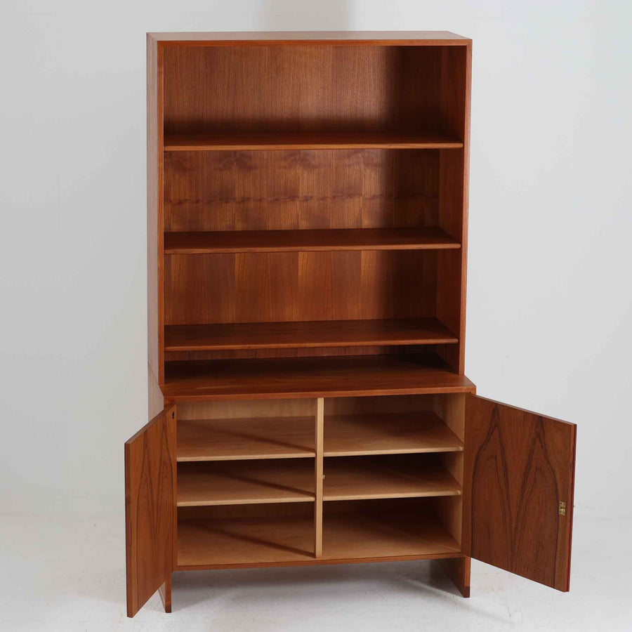 デンマークの巨匠Hans J. Wegner（ハンス・J・ウェグナー）がRY Mobler社のためにデザインしたディスプレイシェルフ「RY5 / RY15」です。上質なチーク材とオーク材を組み合わせ、下段収納部の取手には真鍮を用いた精緻なつくりが特徴です。シンプルながらも素材の美しさが際立ち、ウェグナーらしい温かみのあるデザインに仕上がっています。上段の棚は高さ調整が可能で、下段には仕切り付きの収納スペースを備え、実用性にも優れます。経年により深みを増した木肌の風合いが美しく、リビングや書斎で本や器を飾るなど、多用途に活躍する北欧ビンテージ家具です。