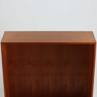 デンマークの巨匠Hans J. Wegner（ハンス・J・ウェグナー）がRY Mobler社のためにデザインしたディスプレイシェルフ「RY5 / RY15」です。上質なチーク材とオーク材を組み合わせ、下段収納部の取手には真鍮を用いた精緻なつくりが特徴です。シンプルながらも素材の美しさが際立ち、ウェグナーらしい温かみのあるデザインに仕上がっています。上段の棚は高さ調整が可能で、下段には仕切り付きの収納スペースを備え、実用性にも優れます。経年により深みを増した木肌の風合いが美しく、リビングや書斎で本や器を飾るなど、多用途に活躍する北欧ビンテージ家具です。