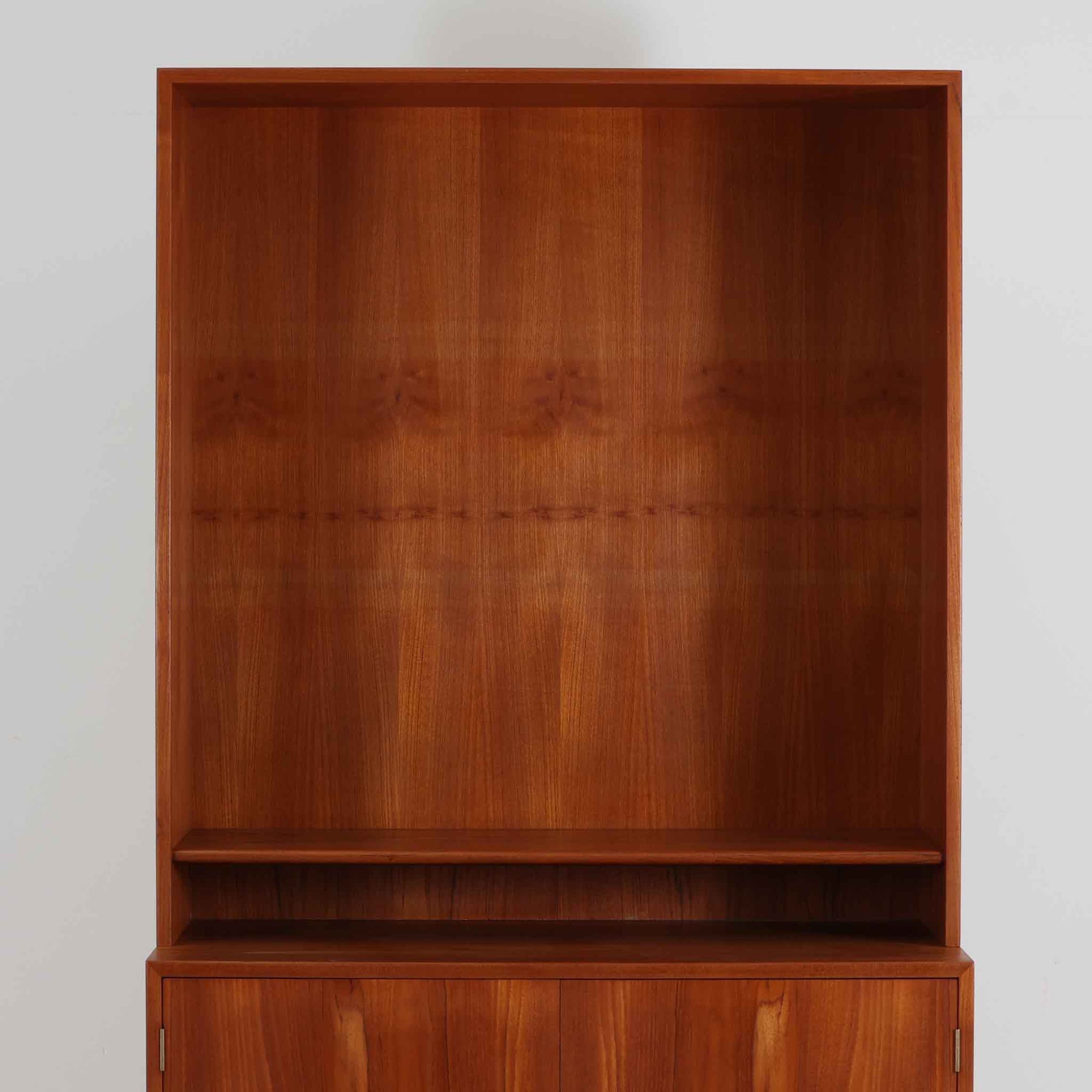 デンマークの巨匠Hans J. Wegner（ハンス・J・ウェグナー）がRY Mobler社のためにデザインしたディスプレイシェルフ「RY5 / RY15」です。上質なチーク材とオーク材を組み合わせ、下段収納部の取手には真鍮を用いた精緻なつくりが特徴です。シンプルながらも素材の美しさが際立ち、ウェグナーらしい温かみのあるデザインに仕上がっています。上段の棚は高さ調整が可能で、下段には仕切り付きの収納スペースを備え、実用性にも優れます。経年により深みを増した木肌の風合いが美しく、リビングや書斎で本や器を飾るなど、多用途に活躍する北欧ビンテージ家具です。