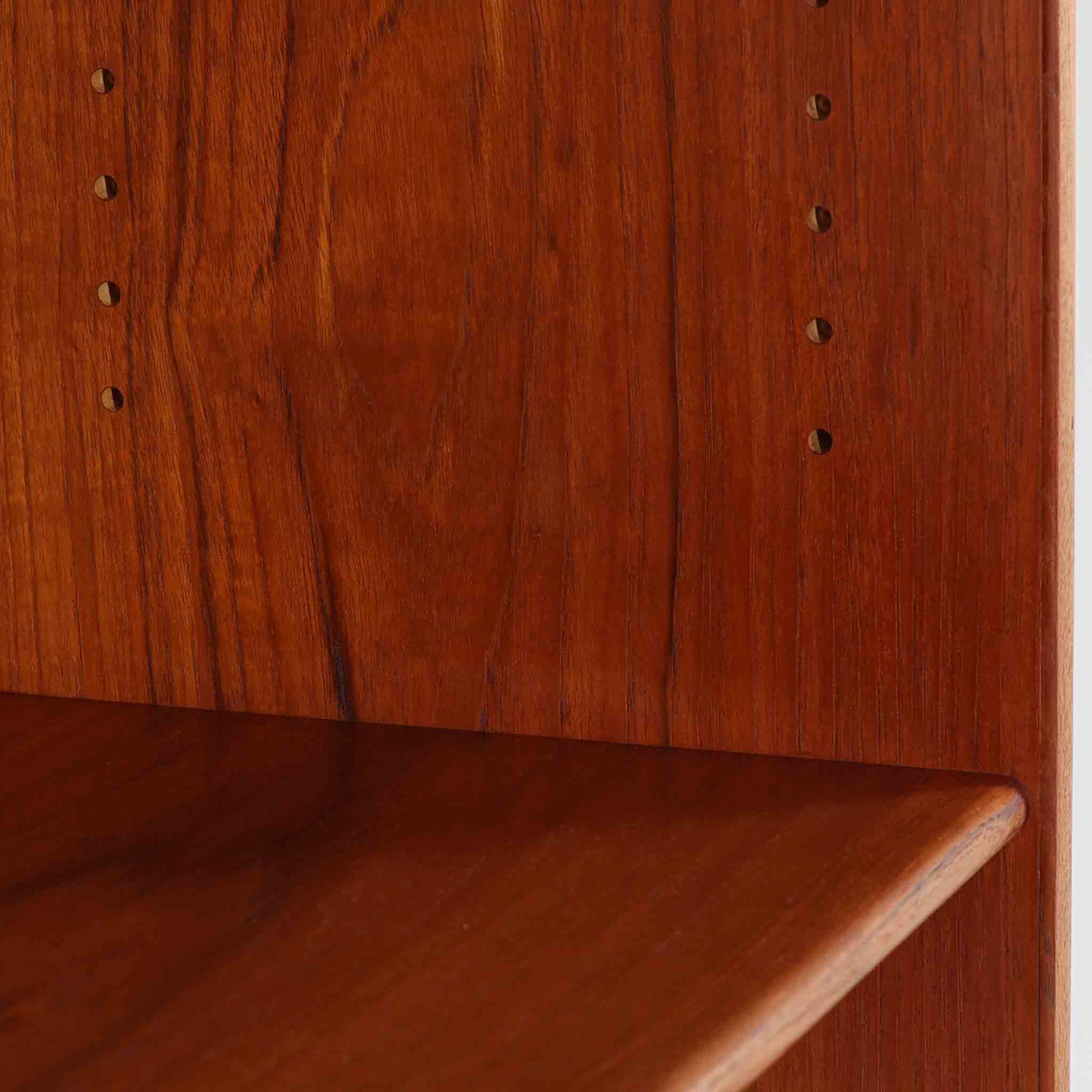 デンマークの巨匠Hans J. Wegner（ハンス・J・ウェグナー）がRY Mobler社のためにデザインしたディスプレイシェルフ「RY5 / RY15」です。上質なチーク材とオーク材を組み合わせ、下段収納部の取手には真鍮を用いた精緻なつくりが特徴です。シンプルながらも素材の美しさが際立ち、ウェグナーらしい温かみのあるデザインに仕上がっています。上段の棚は高さ調整が可能で、下段には仕切り付きの収納スペースを備え、実用性にも優れます。経年により深みを増した木肌の風合いが美しく、リビングや書斎で本や器を飾るなど、多用途に活躍する北欧ビンテージ家具です。