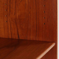 デンマークの巨匠Hans J. Wegner（ハンス・J・ウェグナー）がRY Mobler社のためにデザインしたディスプレイシェルフ「RY5 / RY15」です。上質なチーク材とオーク材を組み合わせ、下段収納部の取手には真鍮を用いた精緻なつくりが特徴です。シンプルながらも素材の美しさが際立ち、ウェグナーらしい温かみのあるデザインに仕上がっています。上段の棚は高さ調整が可能で、下段には仕切り付きの収納スペースを備え、実用性にも優れます。経年により深みを増した木肌の風合いが美しく、リビングや書斎で本や器を飾るなど、多用途に活躍する北欧ビンテージ家具です。