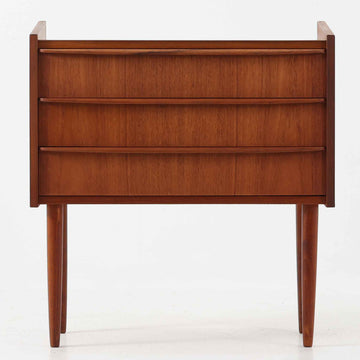 チーク材を使用したデンマーク製の3段チェストで、直線的な本体に対して丸みを帯びた引き手と細身のテーパードレッグが柔らかな印象を与え、さらに天板左右に伸びた耳のような張り出しがデザインのアクセントとなり、北欧らしい優雅な佇まいが感じられます。引き出しは3杯備え、衣類や小物収納に適したサイズ感で、ベッドサイドやリビングの一角に置きやすく、花器や照明のディスプレイ台としても楽しめます。シンプルな造形ながら木目の美しさが際立ち、空間に温かみと落ち着きを添えてくれるビンテージ家具です。