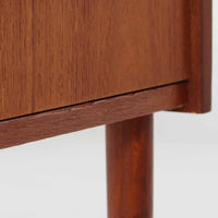 チーク材を使用したデンマーク製の3段チェストで、直線的な本体に対して丸みを帯びた引き手と細身のテーパードレッグが柔らかな印象を与え、さらに天板左右に伸びた耳のような張り出しがデザインのアクセントとなり、北欧らしい優雅な佇まいが感じられます。引き出しは3杯備え、衣類や小物収納に適したサイズ感で、ベッドサイドやリビングの一角に置きやすく、花器や照明のディスプレイ台としても楽しめます。シンプルな造形ながら木目の美しさが際立ち、空間に温かみと落ち着きを添えてくれるビンテージ家具です。