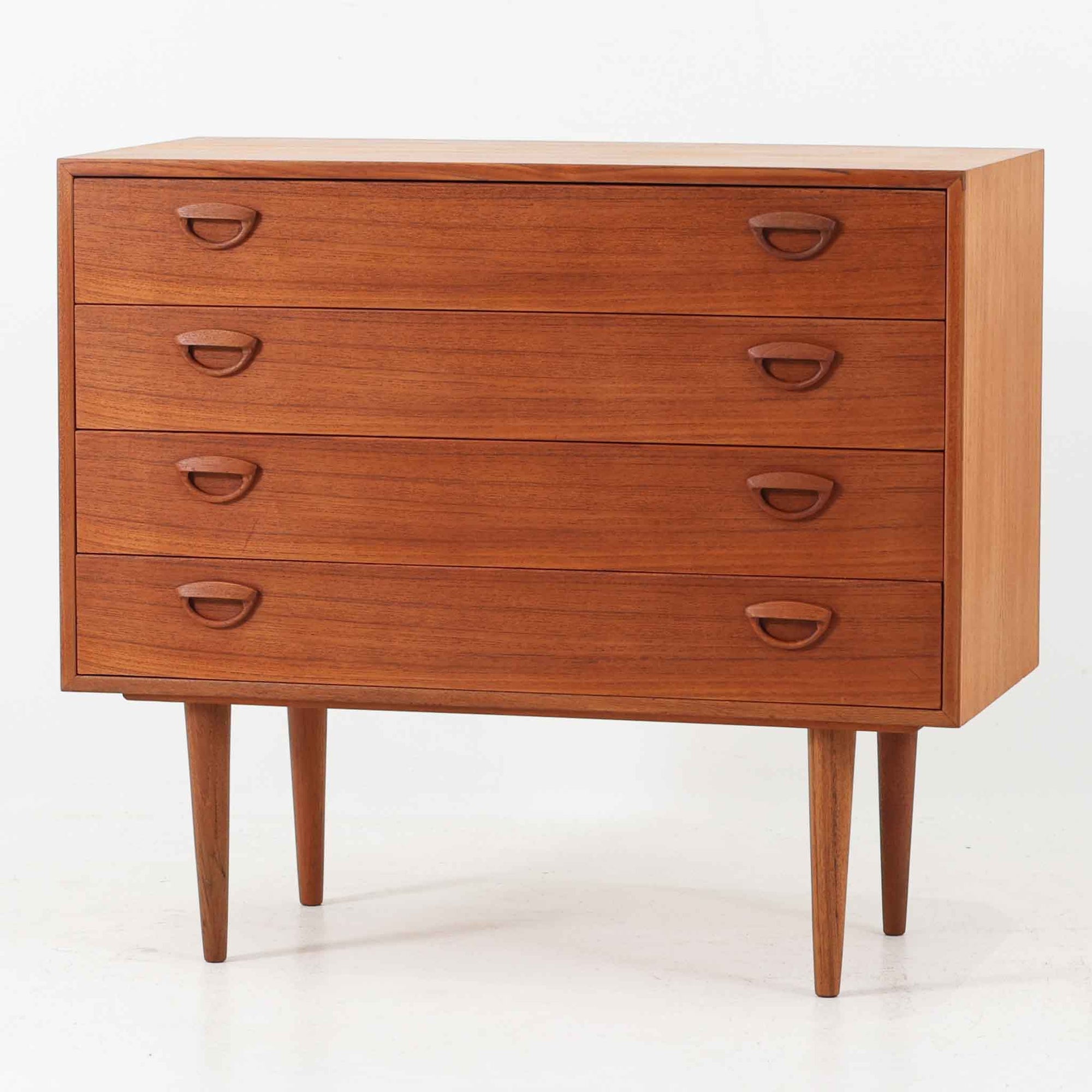 カイ・クリスチャンセンが手掛け、フェルドバレス・モーベルファブリック社によって製作された4段チェストは、北欧ビンテージらしい端正な佇まいと高い実用性を兼ね備えた一台です。良質なチーク材を用いた本体は、木目の美しさが前面に表れ、半円状に削り出された取手や細身のテーパードレッグが、全体に軽やかで洗練された印象を与えています。引き出しは深さにゆとりがあり収納力も十分で、衣類や小物の整理に最適です。経年変化によって深みを増したチークの色合いが空間に温もりを添え、リビングや寝室、書斎など幅広いシーンで主役として活躍します。