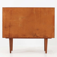 カイ・クリスチャンセンが手掛け、フェルドバレス・モーベルファブリック社によって製作された4段チェストは、北欧ビンテージらしい端正な佇まいと高い実用性を兼ね備えた一台です。良質なチーク材を用いた本体は、木目の美しさが前面に表れ、半円状に削り出された取手や細身のテーパードレッグが、全体に軽やかで洗練された印象を与えています。引き出しは深さにゆとりがあり収納力も十分で、衣類や小物の整理に最適です。経年変化によって深みを増したチークの色合いが空間に温もりを添え、リビングや寝室、書斎など幅広いシーンで主役として活躍します。