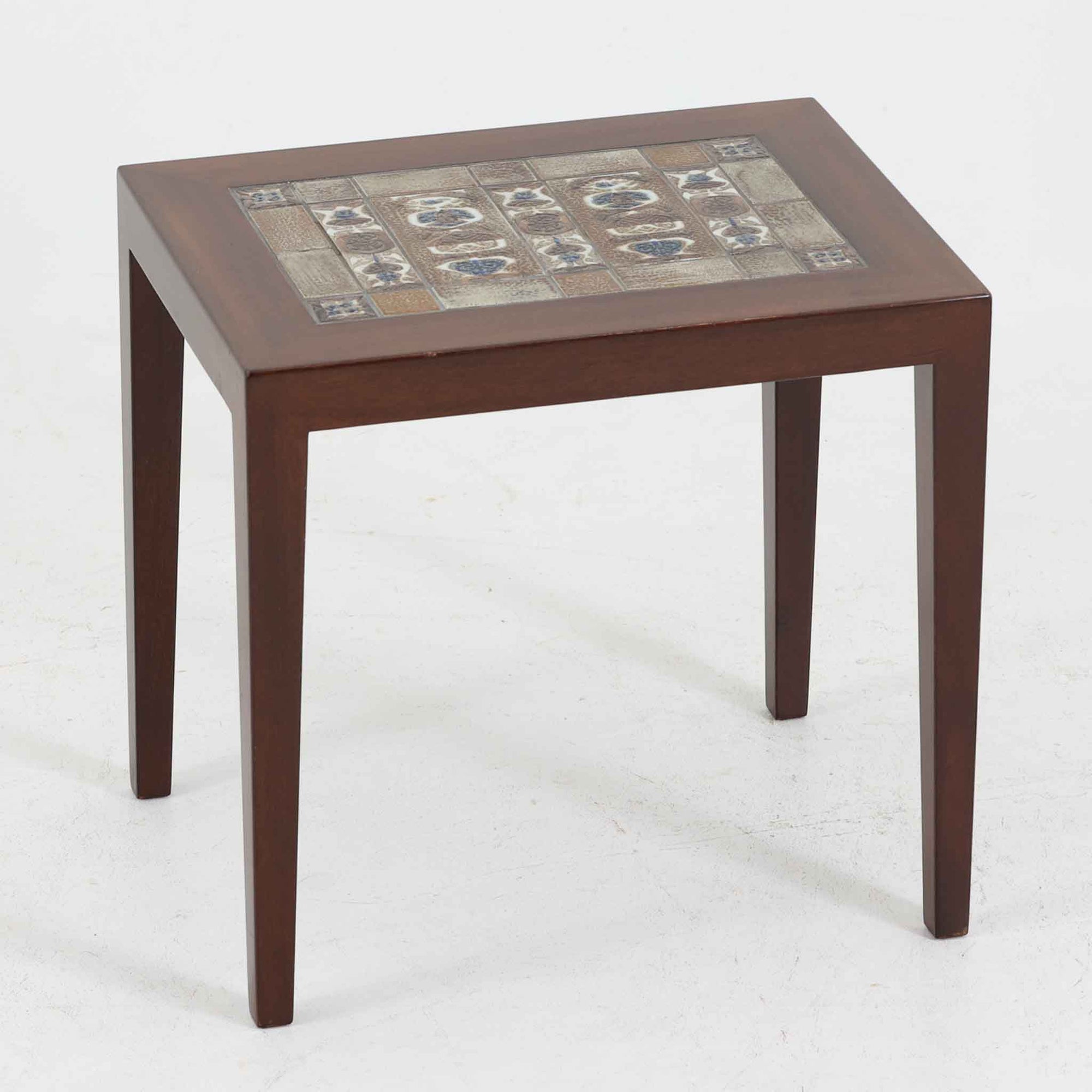 Severin Hansen Jr.（セヴェリン・ハンセン）がデザインし、Haslev社より製造されたタイルトップテーブルで、天板にはNils ThorssonによるBACAシリーズの陶板が贅沢にあしらわれています。端正な角脚を持つマホガニー材のフレームは、ハンセンらしいシャープなジョイントが際立ち、凛とした佇まいを演出します。耐熱性に優れたタイルは日常使いに適しており、サイドテーブルや植物のディスプレイスペースとしても活躍。経年により深みを増した木肌とBACA特有の芸術性が空間に上質なアクセントを添えるビンテージ品です。