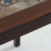 Severin Hansen Jr.（セヴェリン・ハンセン）がデザインし、Haslev社より製造されたタイルトップテーブルで、天板にはNils ThorssonによるBACAシリーズの陶板が贅沢にあしらわれています。端正な角脚を持つマホガニー材のフレームは、ハンセンらしいシャープなジョイントが際立ち、凛とした佇まいを演出します。耐熱性に優れたタイルは日常使いに適しており、サイドテーブルや植物のディスプレイスペースとしても活躍。経年により深みを増した木肌とBACA特有の芸術性が空間に上質なアクセントを添えるビンテージ品です。