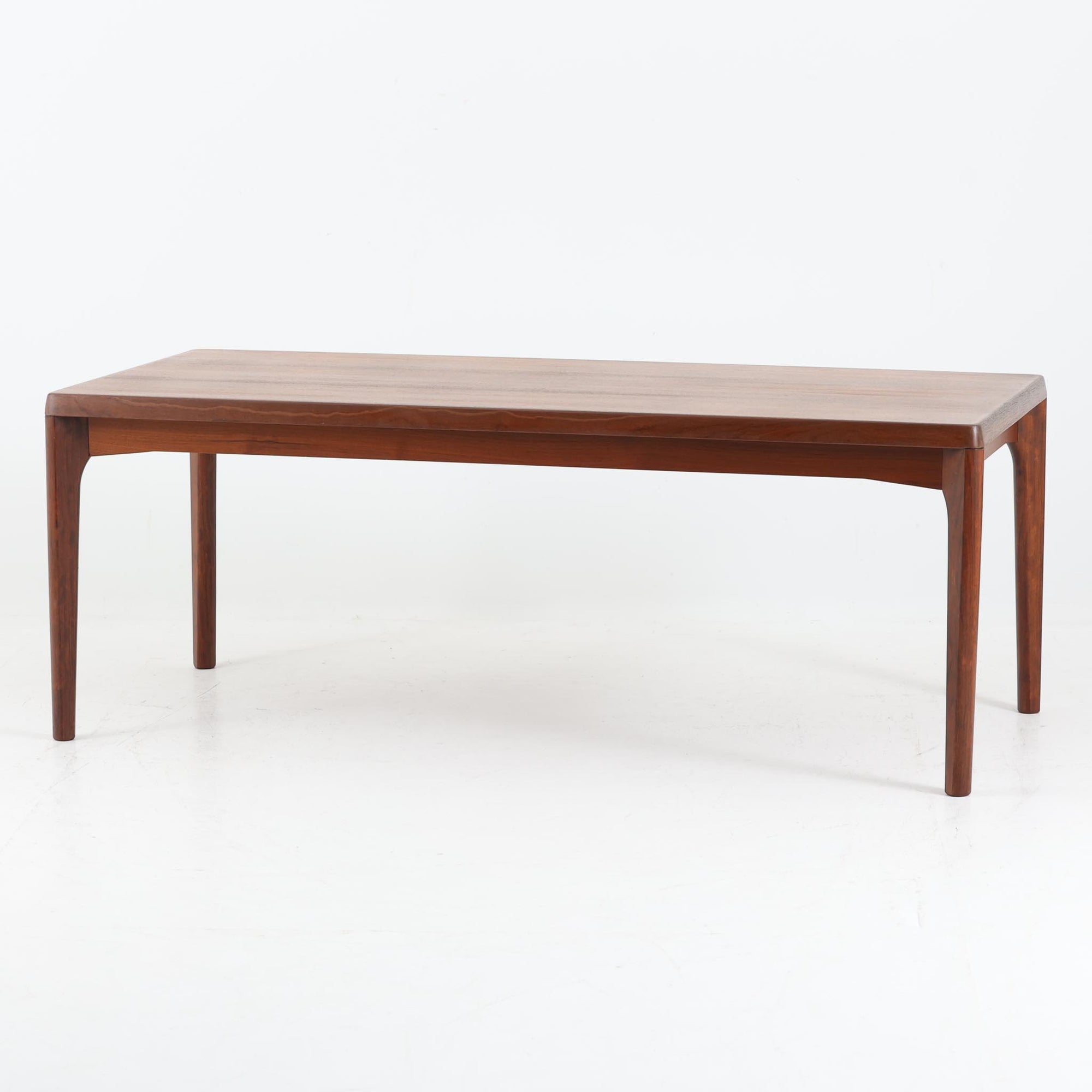 Henning Kjaernulf（ヘニング・ケアヌルフ）によるデザイン、Vejle Stole og Mobelfabrik社製のセンターテーブルです。チーク材特有の深みある色合いと美しい木目が際立ち、北欧家具らしい上質な雰囲気を漂わせます。脚部から幕板にかけての滑らかな曲線が職人技を感じさせ、どの角度から見ても整った美しいフォルムが魅力です。リビングの中心で穏やかな存在感を放ち、ソファとの相性も抜群。経年により増した艶が、ビンテージ家具ならではの温もりを感じさせます。なお、天板や幕板はチーク材と思われ、脚部にはチークに近い色調と質感をもつアフロモシア材が使用されている可能性があります。