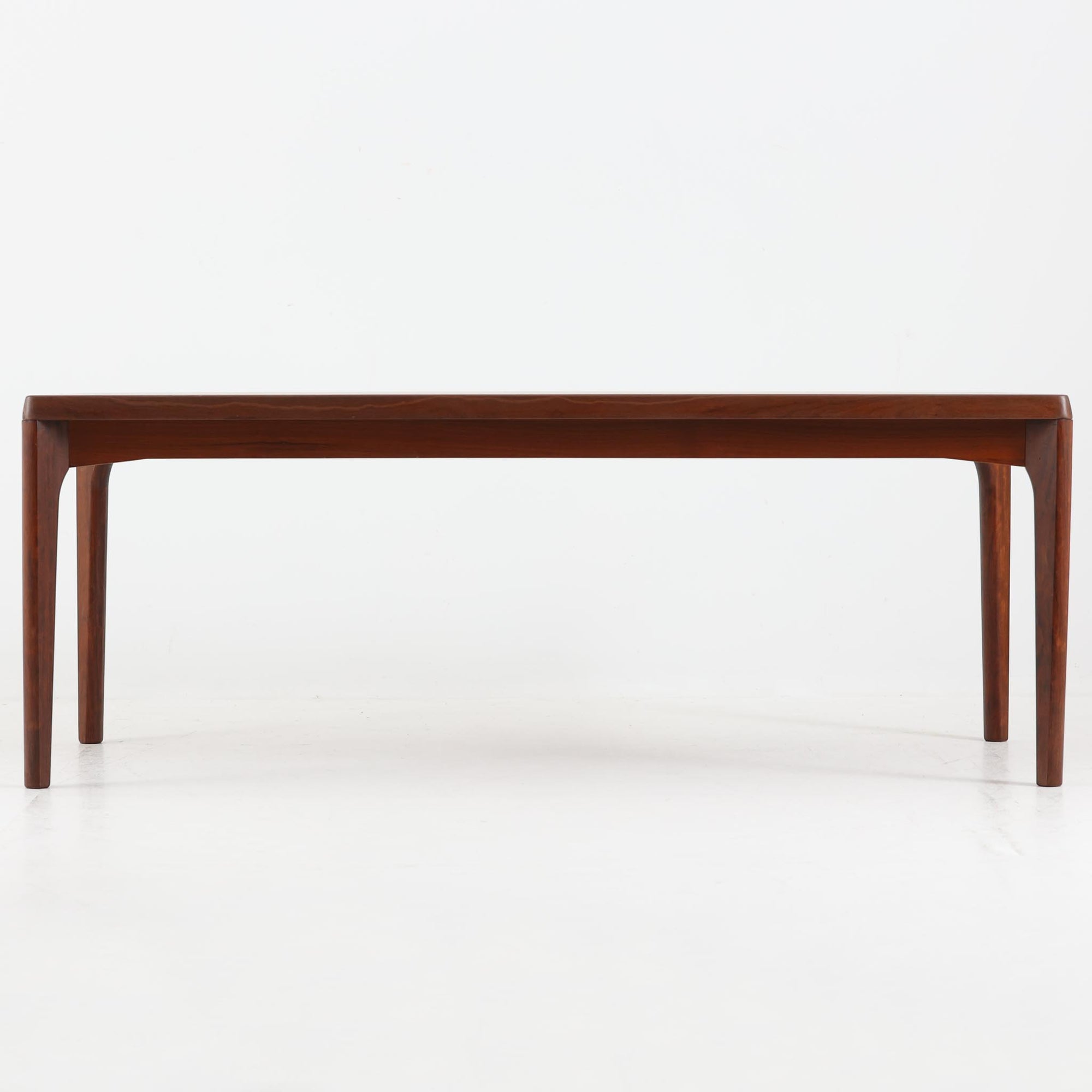 Henning Kjaernulf（ヘニング・ケアヌルフ）によるデザイン、Vejle Stole og Mobelfabrik社製のセンターテーブルです。チーク材特有の深みある色合いと美しい木目が際立ち、北欧家具らしい上質な雰囲気を漂わせます。脚部から幕板にかけての滑らかな曲線が職人技を感じさせ、どの角度から見ても整った美しいフォルムが魅力です。リビングの中心で穏やかな存在感を放ち、ソファとの相性も抜群。経年により増した艶が、ビンテージ家具ならではの温もりを感じさせます。なお、天板や幕板はチーク材と思われ、脚部にはチークに近い色調と質感をもつアフロモシア材が使用されている可能性があります。