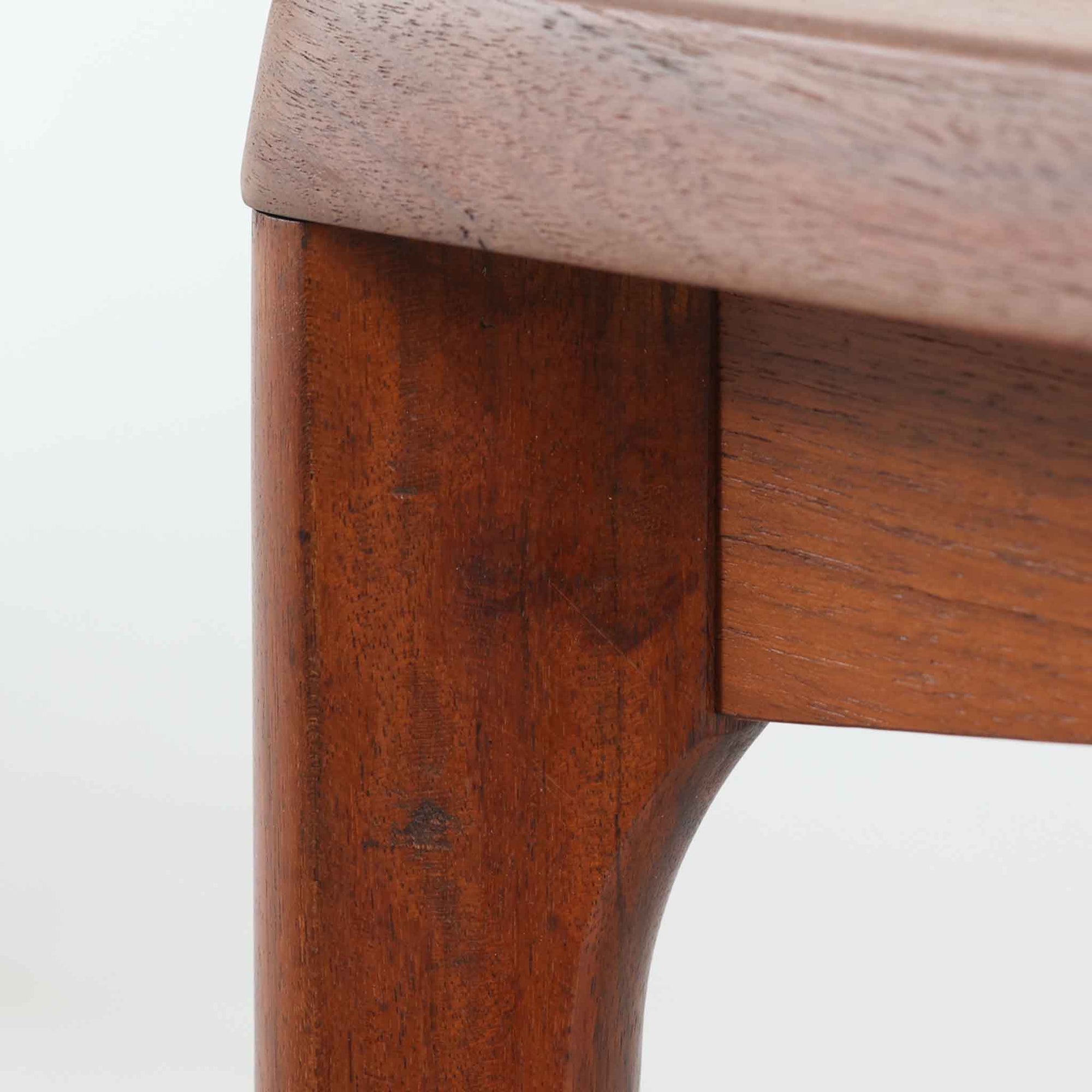 Henning Kjaernulf（ヘニング・ケアヌルフ）によるデザイン、Vejle Stole og Mobelfabrik社製のセンターテーブルです。チーク材特有の深みある色合いと美しい木目が際立ち、北欧家具らしい上質な雰囲気を漂わせます。脚部から幕板にかけての滑らかな曲線が職人技を感じさせ、どの角度から見ても整った美しいフォルムが魅力です。リビングの中心で穏やかな存在感を放ち、ソファとの相性も抜群。経年により増した艶が、ビンテージ家具ならではの温もりを感じさせます。なお、天板や幕板はチーク材と思われ、脚部にはチークに近い色調と質感をもつアフロモシア材が使用されている可能性があります。