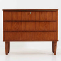 デンマーク製のチーク材3段チェストです。前板の一体的なデザインが美しく、取手部分を削り出した滑らかなラインが上品な印象を与えます。幅が77cmと少し大きめで、コンパクトながら収納力があり、寝室や玄関、リビングのサイド収納としても活躍します。最上段には鍵付きの引き出しが設けられ、大切な書類や貴重品の保管にも便利です。脚部まで丁寧に仕上げられた造りは北欧家具ならではの職人技を感じさせ、空間に温もりを添えてくれます。