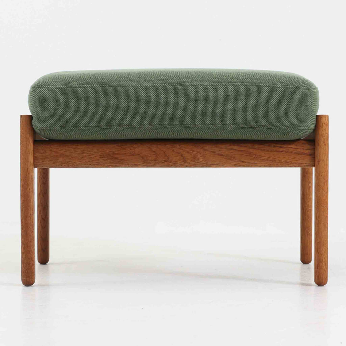 ハンス・J・ウェグナーがデザインし、ゲタマ社から発表されたGE290オットマンは、堅牢なオーク材のフレームと、ウール混紡のざっくりとした風合いを持つ落ち着いたグリーン系の張地が美しく調和した北欧ビンテージ家具です。直線的でありながら丸みを帯びた脚部が軽快な印象を与え、ソファと組み合わせてフットレストとして、あるいは単体で腰掛けとしてもお使いいただけます。経年によって深まった木肌の風合いと上質な張地が空間に落ち着いた存在感をもたらし、クッション内部にはビンテージ品ならではのスプリングが内包されています。