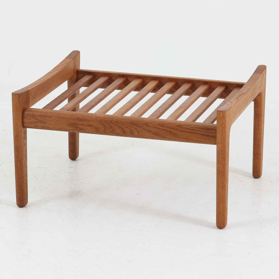 ハンス・J・ウェグナーがデザインし、ゲタマ社から発表されたGE290オットマンは、堅牢なオーク材のフレームと、ウール混紡のざっくりとした風合いを持つ落ち着いたグリーン系の張地が美しく調和した北欧ビンテージ家具です。直線的でありながら丸みを帯びた脚部が軽快な印象を与え、ソファと組み合わせてフットレストとして、あるいは単体で腰掛けとしてもお使いいただけます。経年によって深まった木肌の風合いと上質な張地が空間に落ち着いた存在感をもたらし、クッション内部にはビンテージ品ならではのスプリングが内包されています。