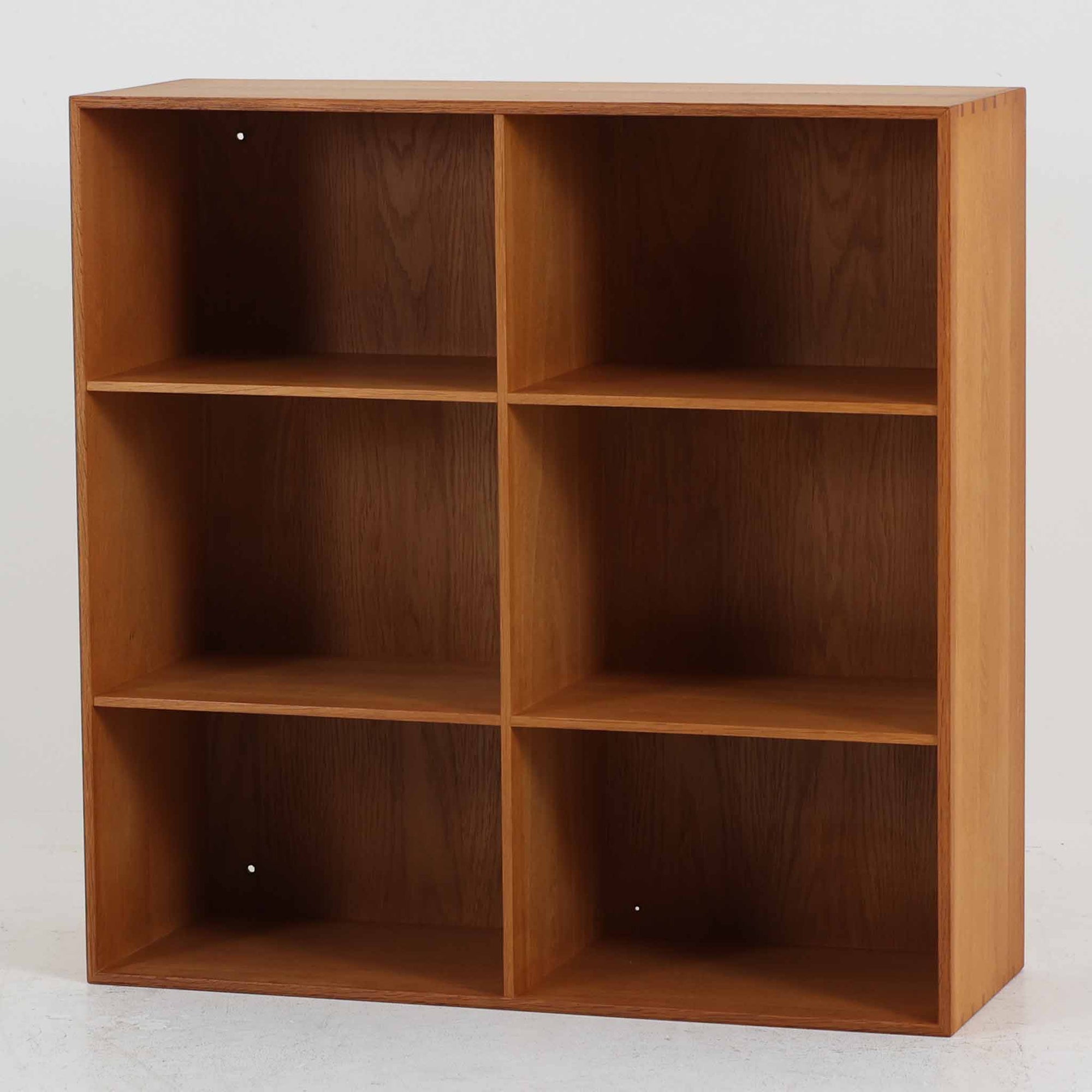 デンマークの建築家Mogens Koch（モーエンス・コッホ）によってデザインされ、名工房Rud. Rasmussen社で製造されたオーク無垢材のブックシェルフです。無駄のない端正なフォルムと精緻な組継ぎ構造が特徴で、堅牢さと美しさを兼ね備えています。ナチュラルなオークの木肌は経年により温かみを増し、シンプルながらも存在感のある佇まいを演出。縦横いずれの向きでも使用でき、複数を組み合わせて自由にレイアウトできる汎用性の高い北欧ビンテージ家具です。
