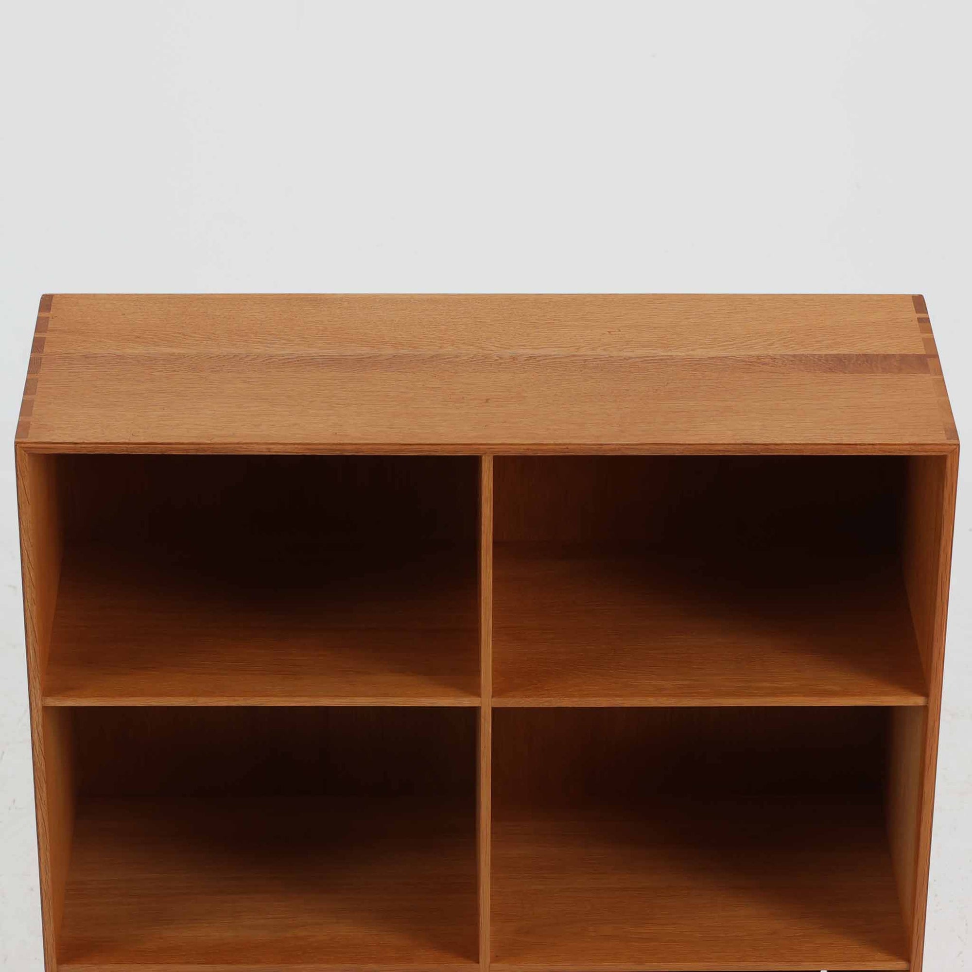 デンマークの建築家Mogens Koch（モーエンス・コッホ）によってデザインされ、名工房Rud. Rasmussen社で製造されたオーク無垢材のブックシェルフです。無駄のない端正なフォルムと精緻な組継ぎ構造が特徴で、堅牢さと美しさを兼ね備えています。ナチュラルなオークの木肌は経年により温かみを増し、シンプルながらも存在感のある佇まいを演出。縦横いずれの向きでも使用でき、複数を組み合わせて自由にレイアウトできる汎用性の高い北欧ビンテージ家具です。